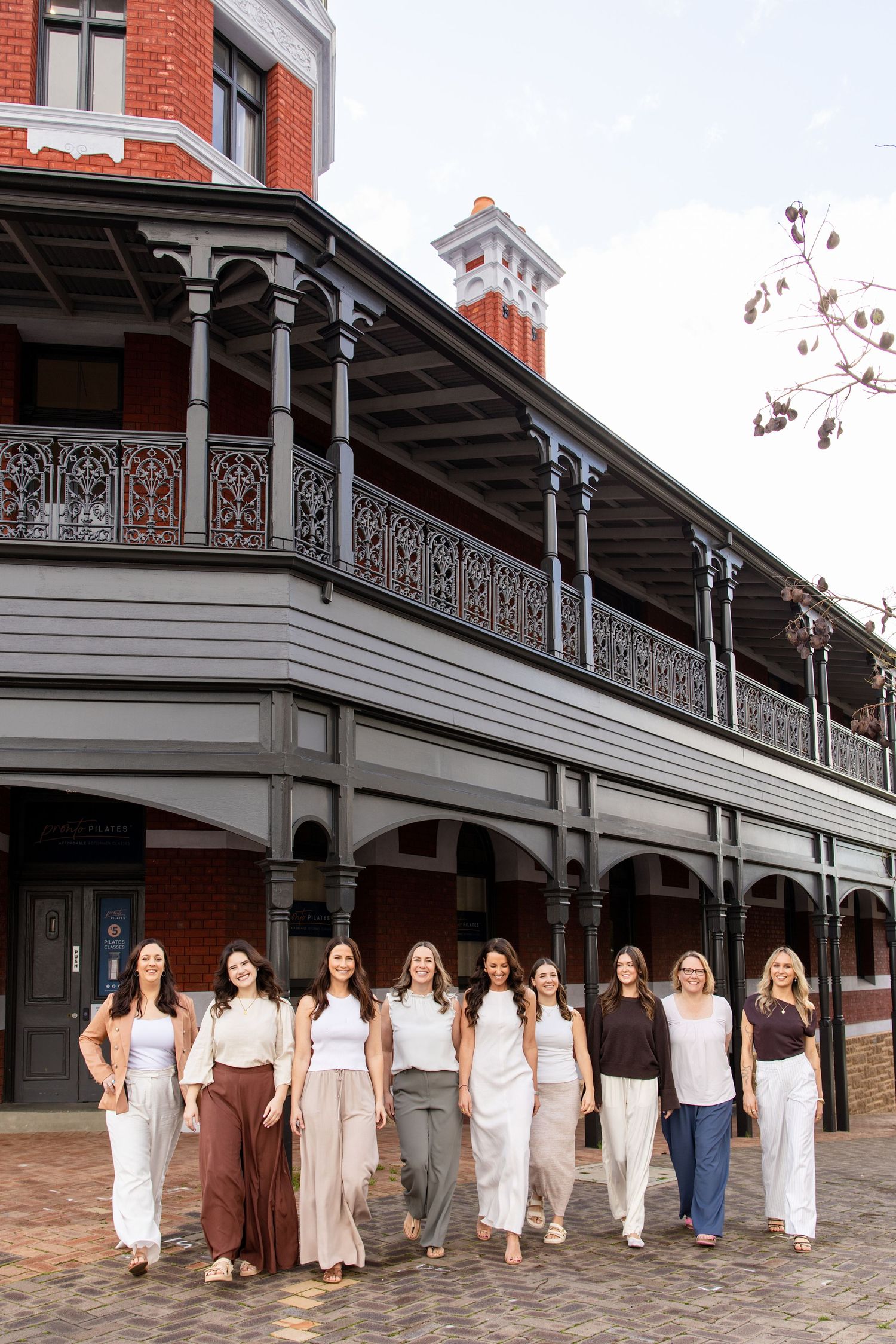 Group of nine women posing in front of a historic Victorian building with ornate iron balcony.