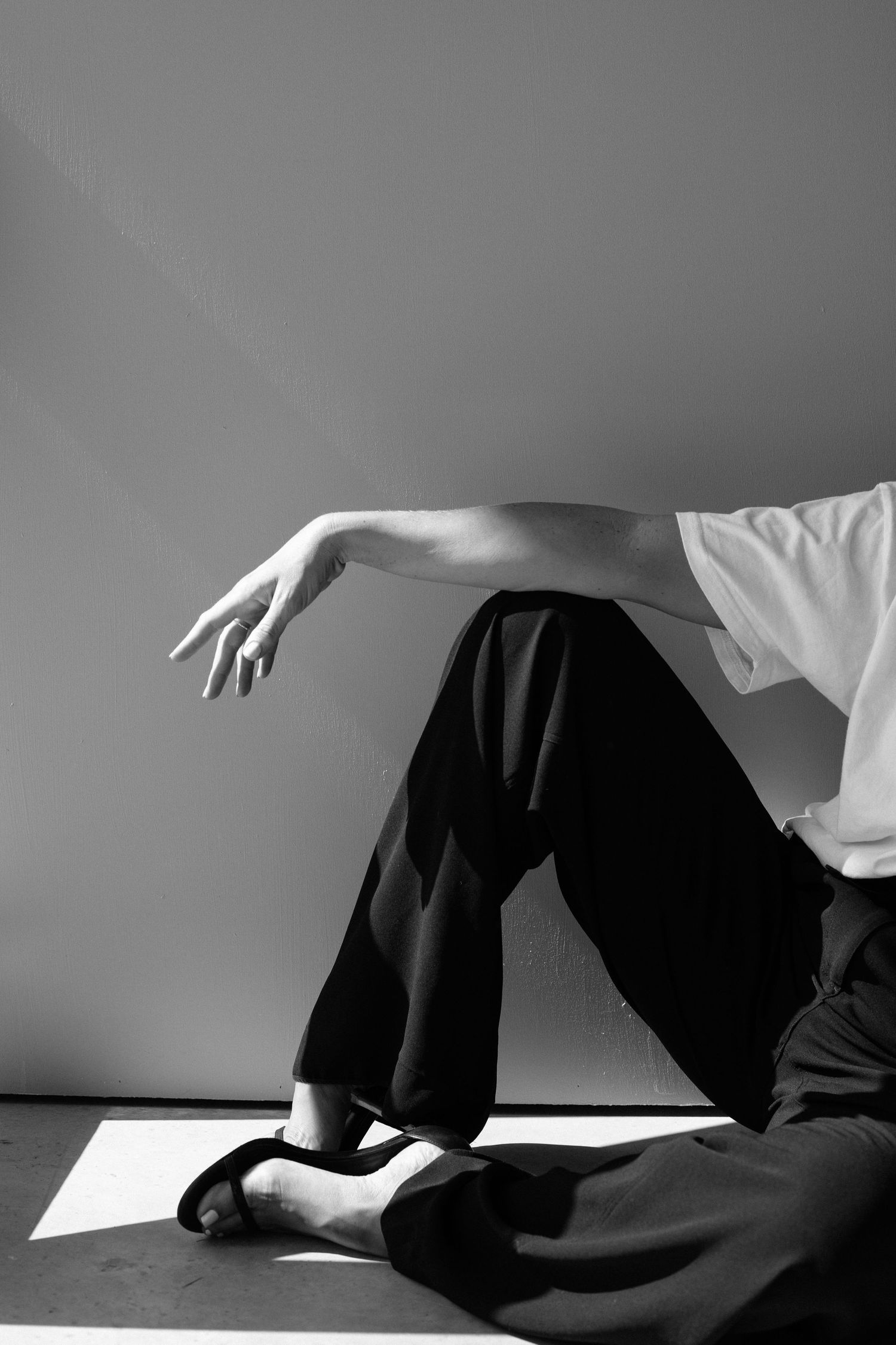 Black and white photo of a person in wide-leg pants and heels, seated on floor with arm elegantly extended.