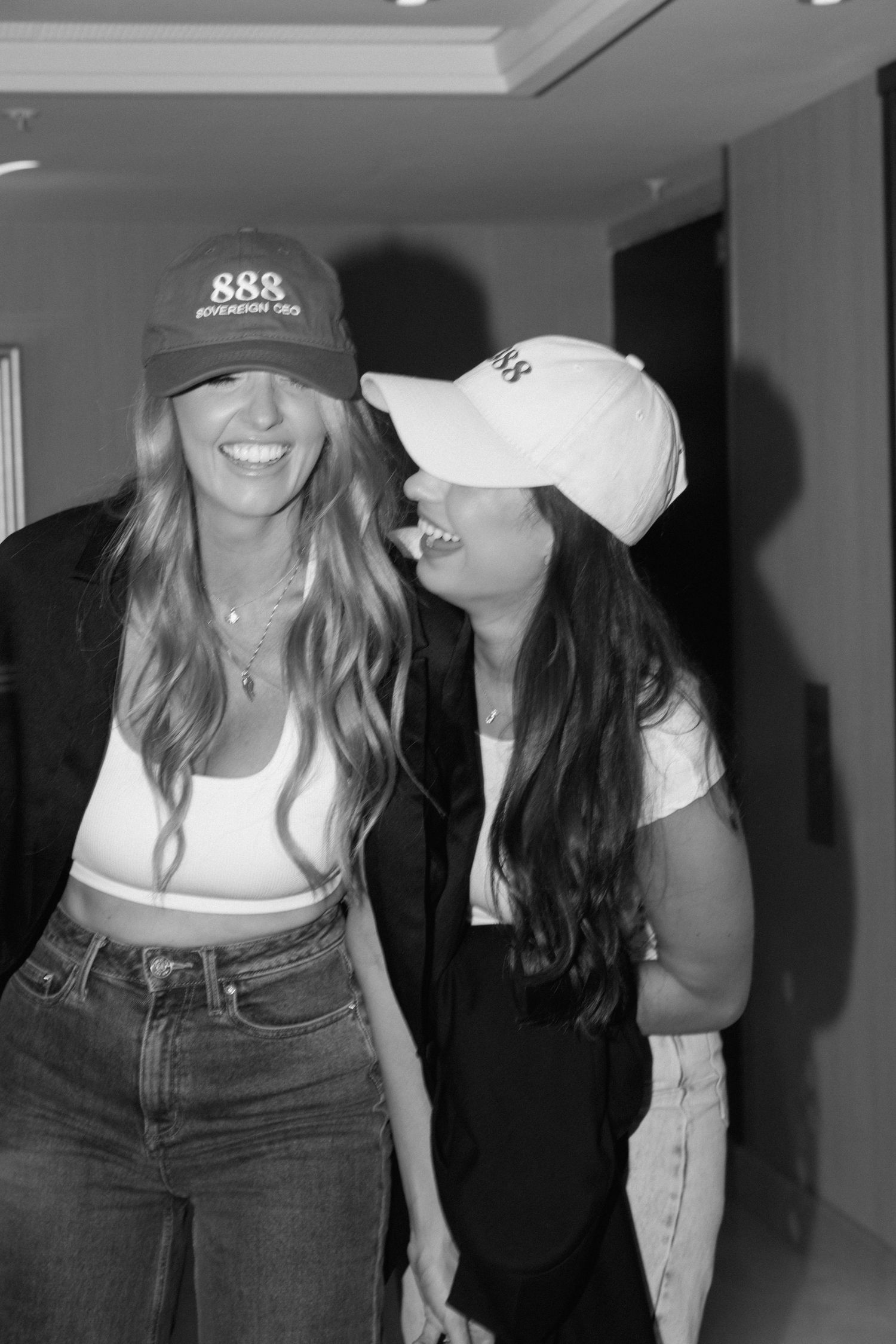 Two people in casual outfits with baseball caps posing together in a dark hallway.