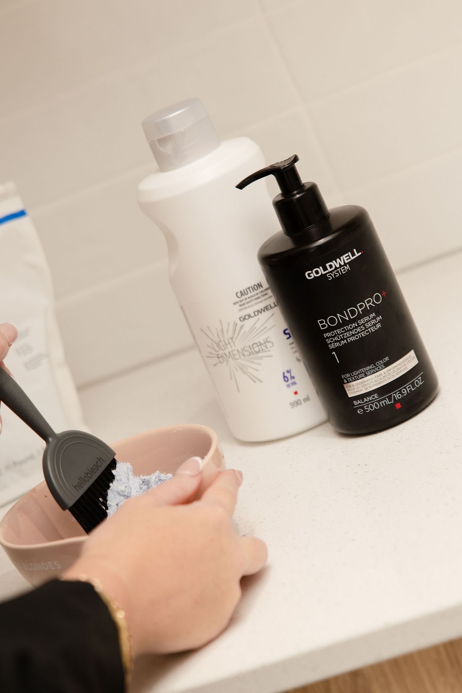 Hair coloring tools with Goldwell BondPro and Criterion shampoo bottles on a white counter.