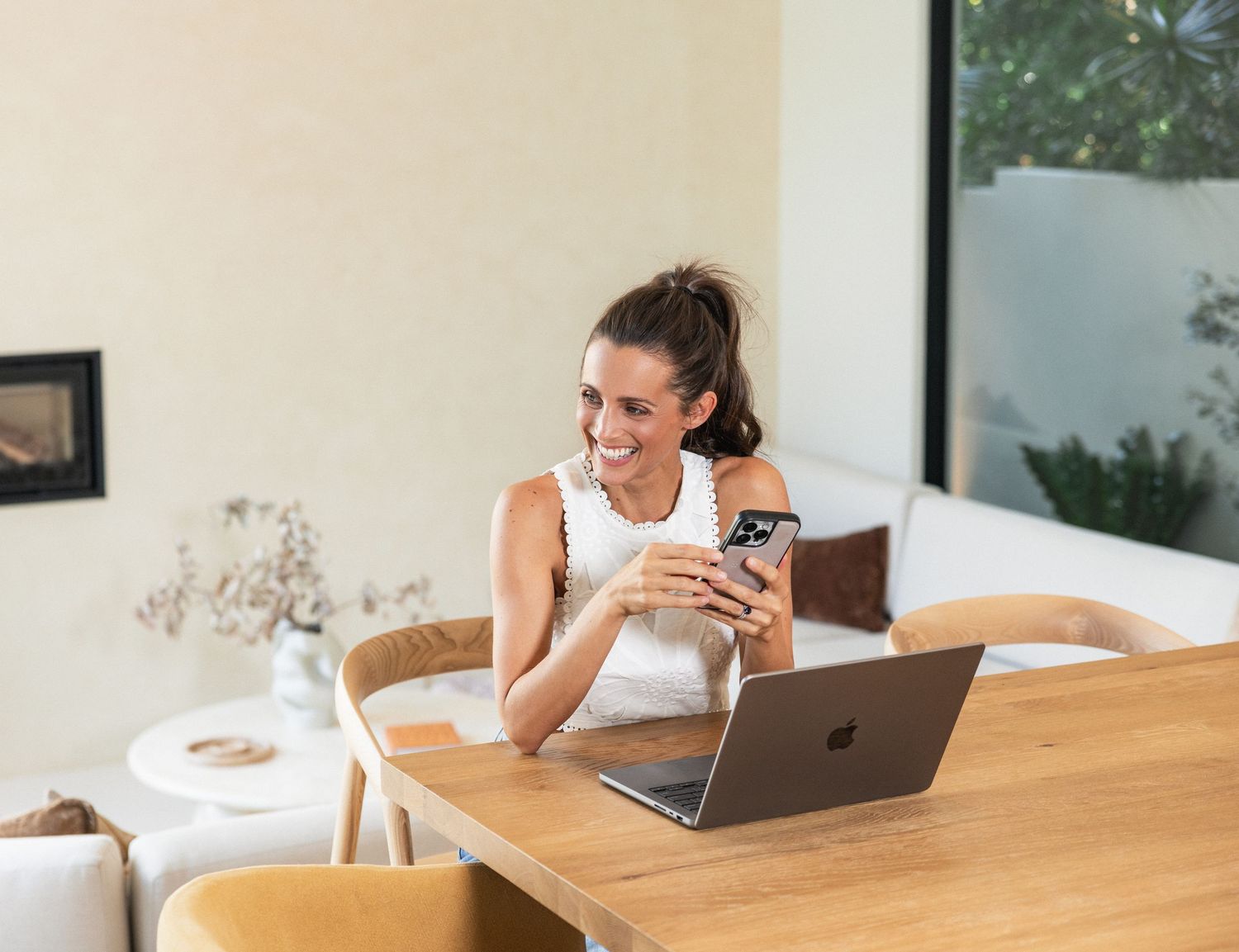 A young woman working on a laptop while sitting at a wooden table in a cozy home environment.