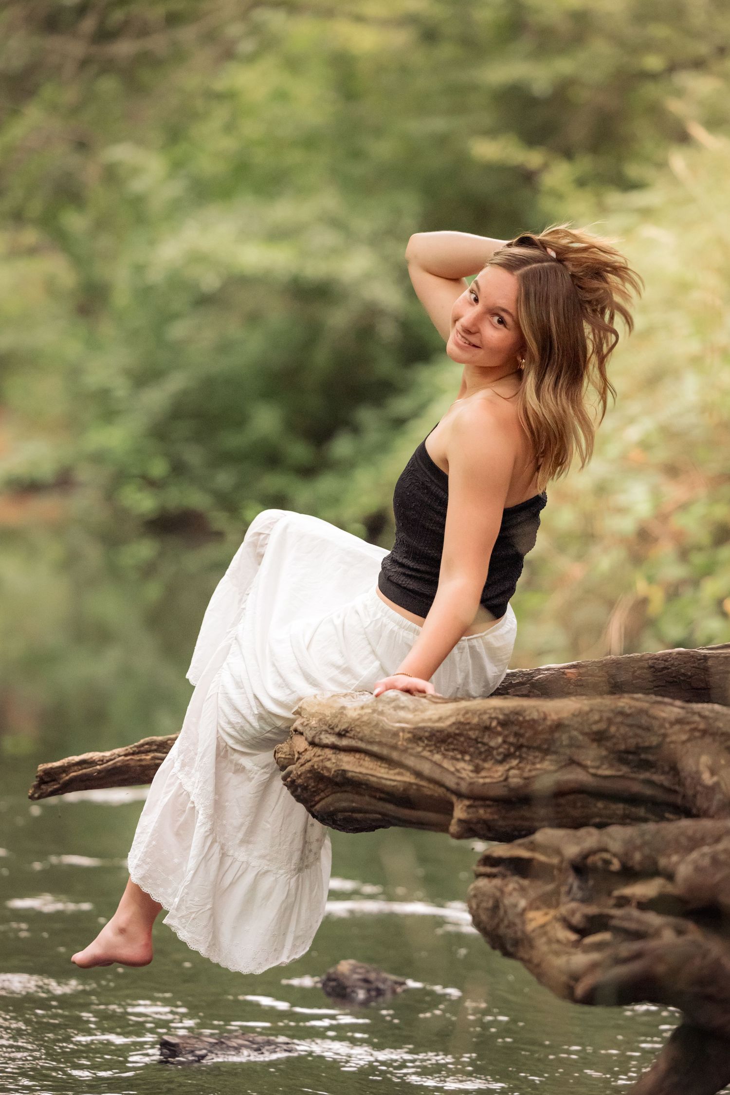 A tranquil scene by a pond with someone resting on a fallen log over the water's surface.