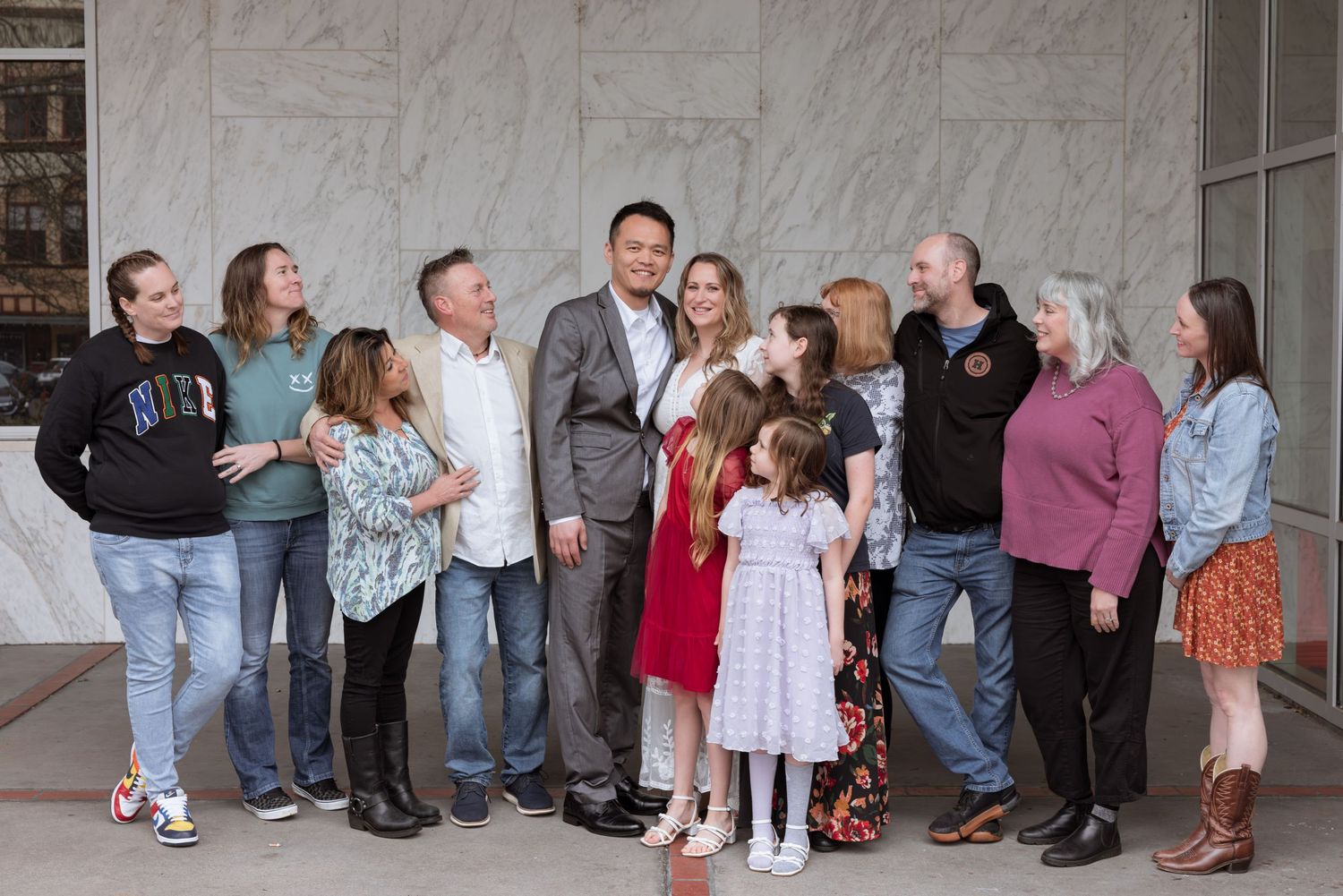 Large family group posing together outdoors in front of a building, smiling for a formal portrait photo.