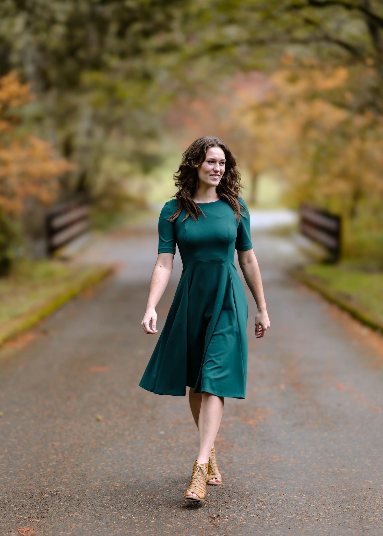 Senior in a teal dress walking along an autumn path surrounded by trees during a photo session taken by Salem, Oregon senior photographer.