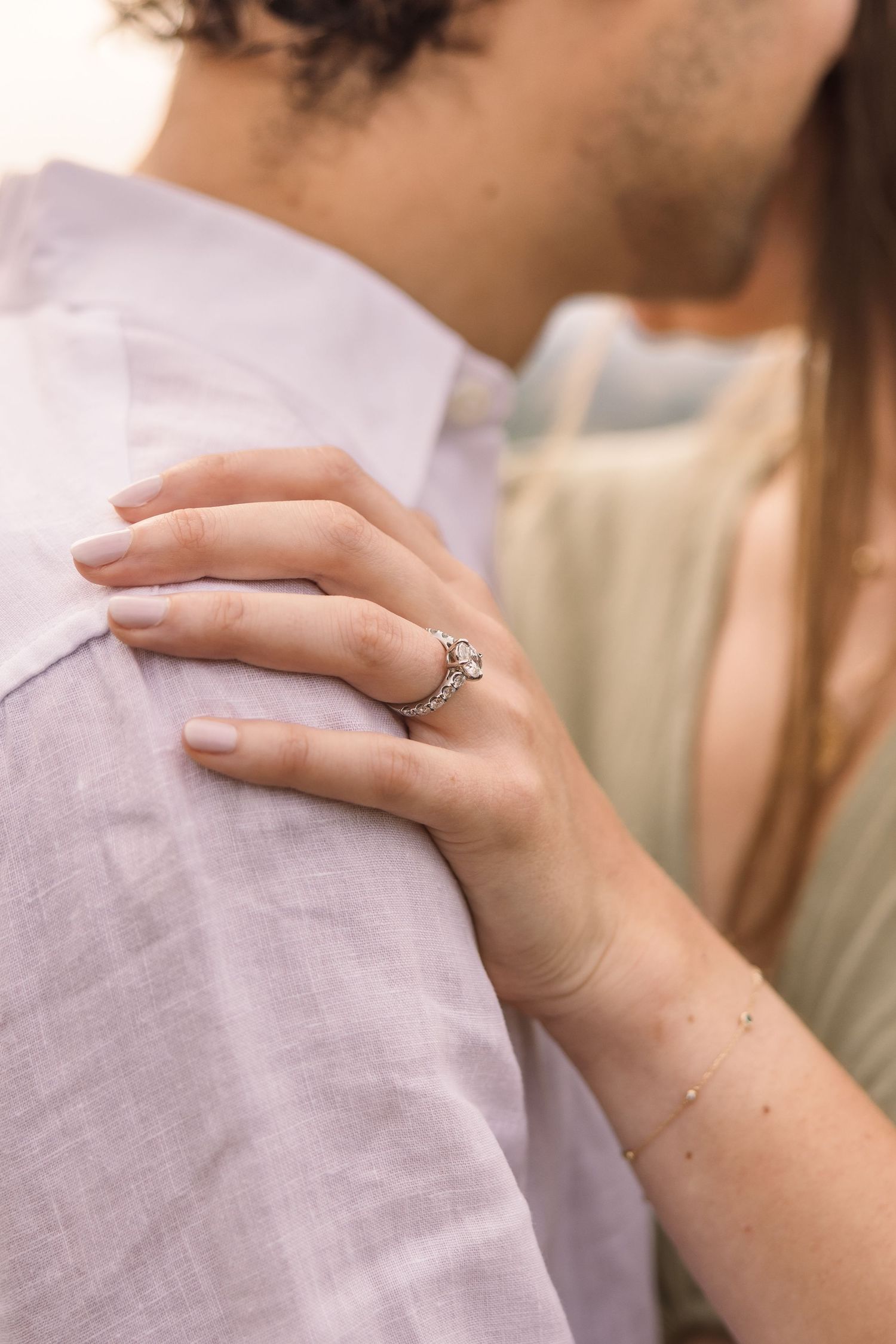Close-up view of a delicate engagement ring on a woman's hand resting against a soft gray fabric background.