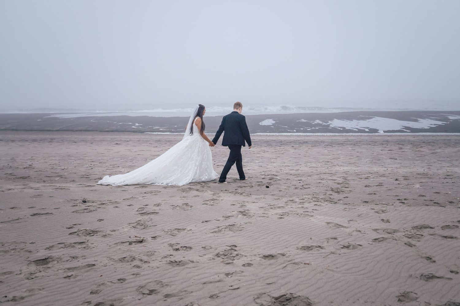 A romantic beach wedding photo session with dramatic cloudy skies and waves in the background.