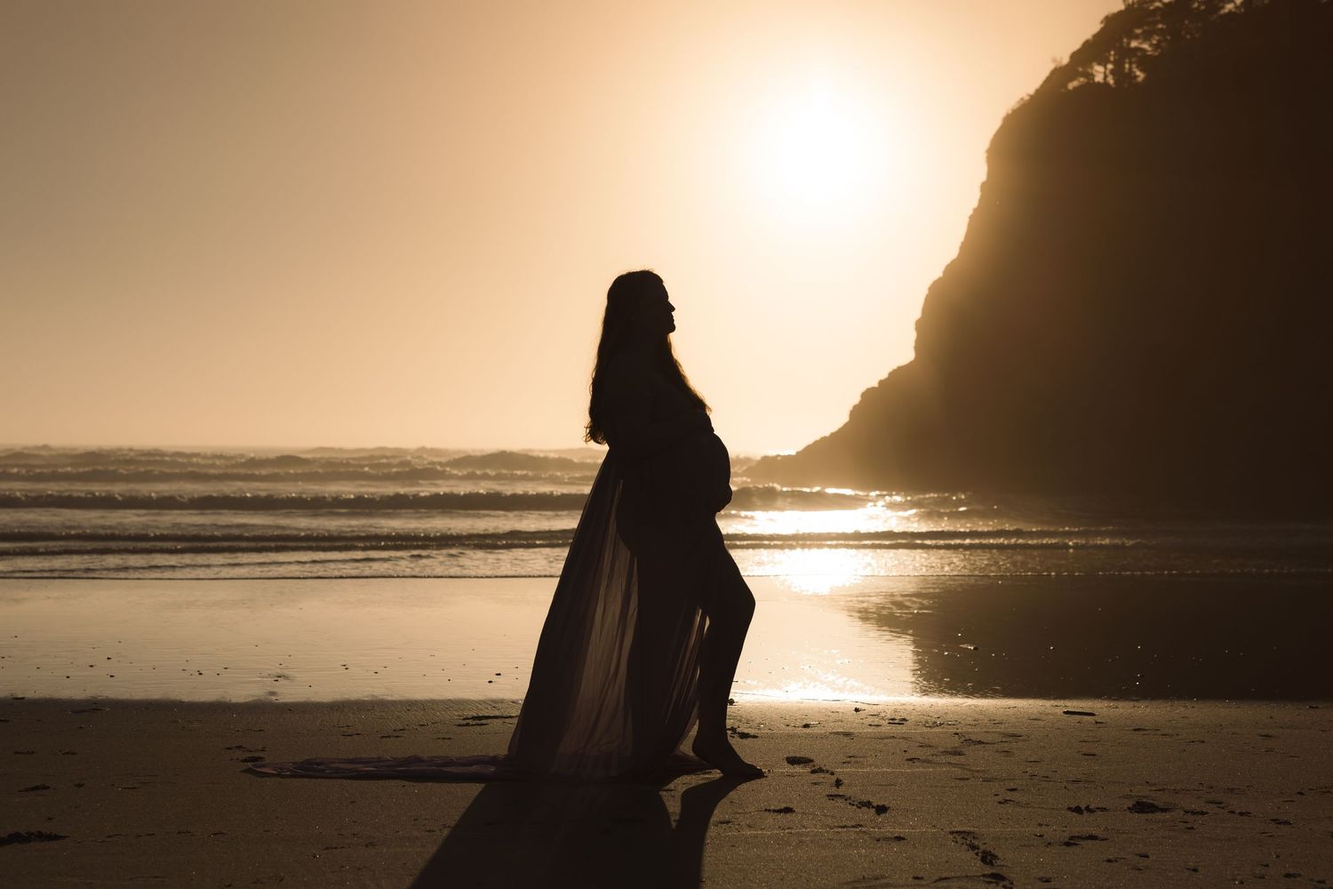 Silhouette of figures walking along a misty beach at sunset with dramatic coastal cliffs in the background.