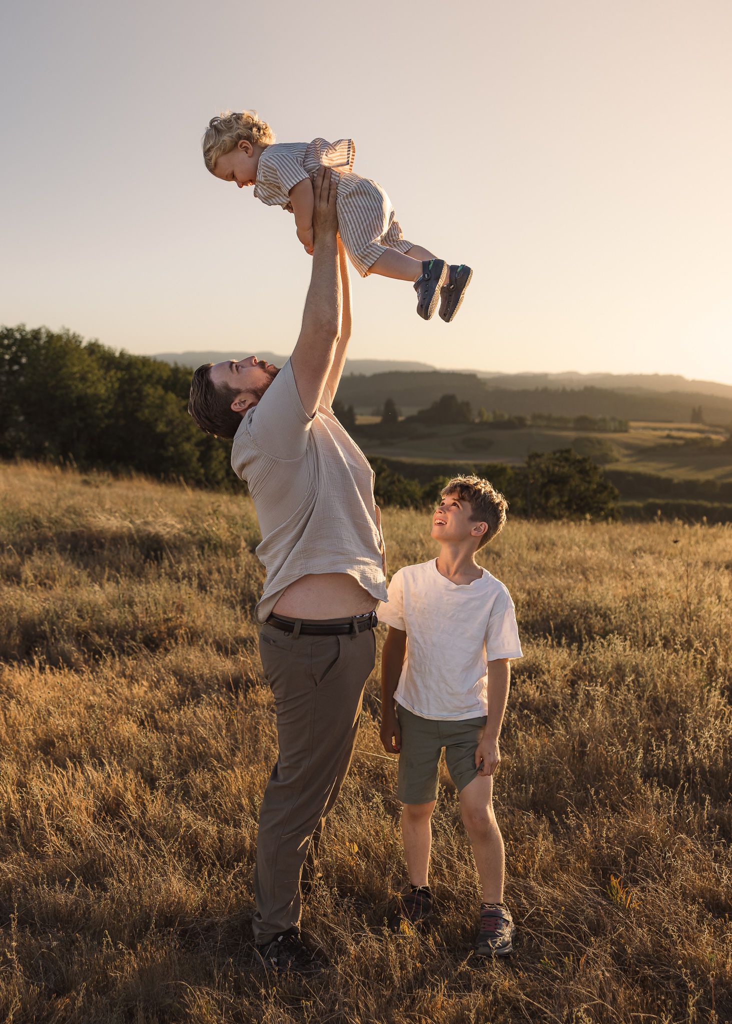 Family in golden field at sunset with child being lifted in the air during a photo session taken by Salem, Oregon family photographer.