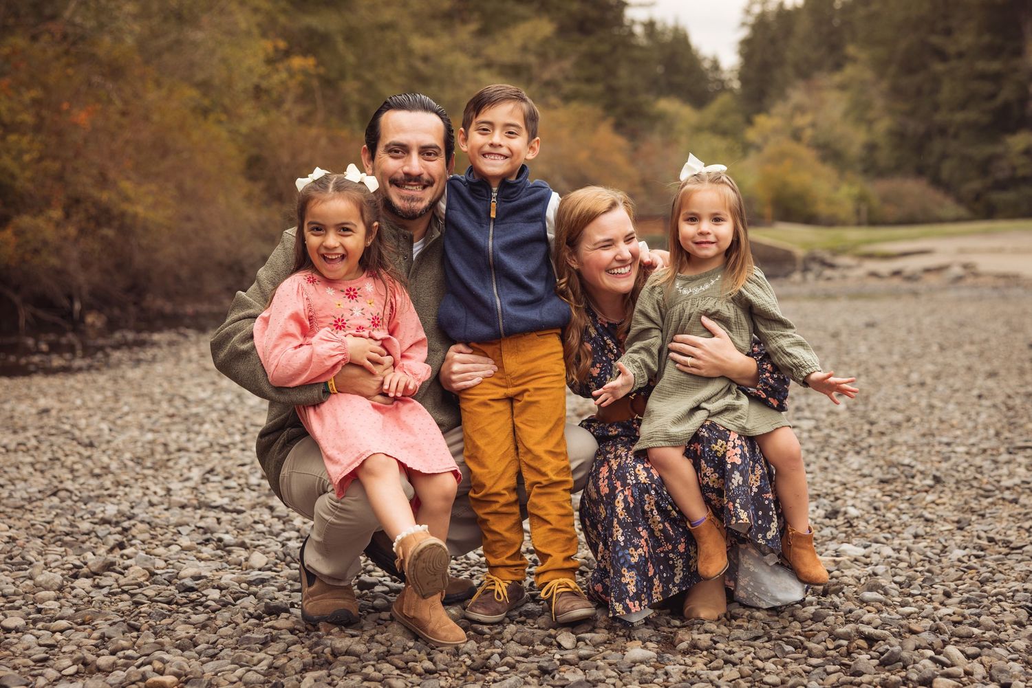 A group sits together on a rocky beach surrounded by autumn trees and foliage during a fall photo session.