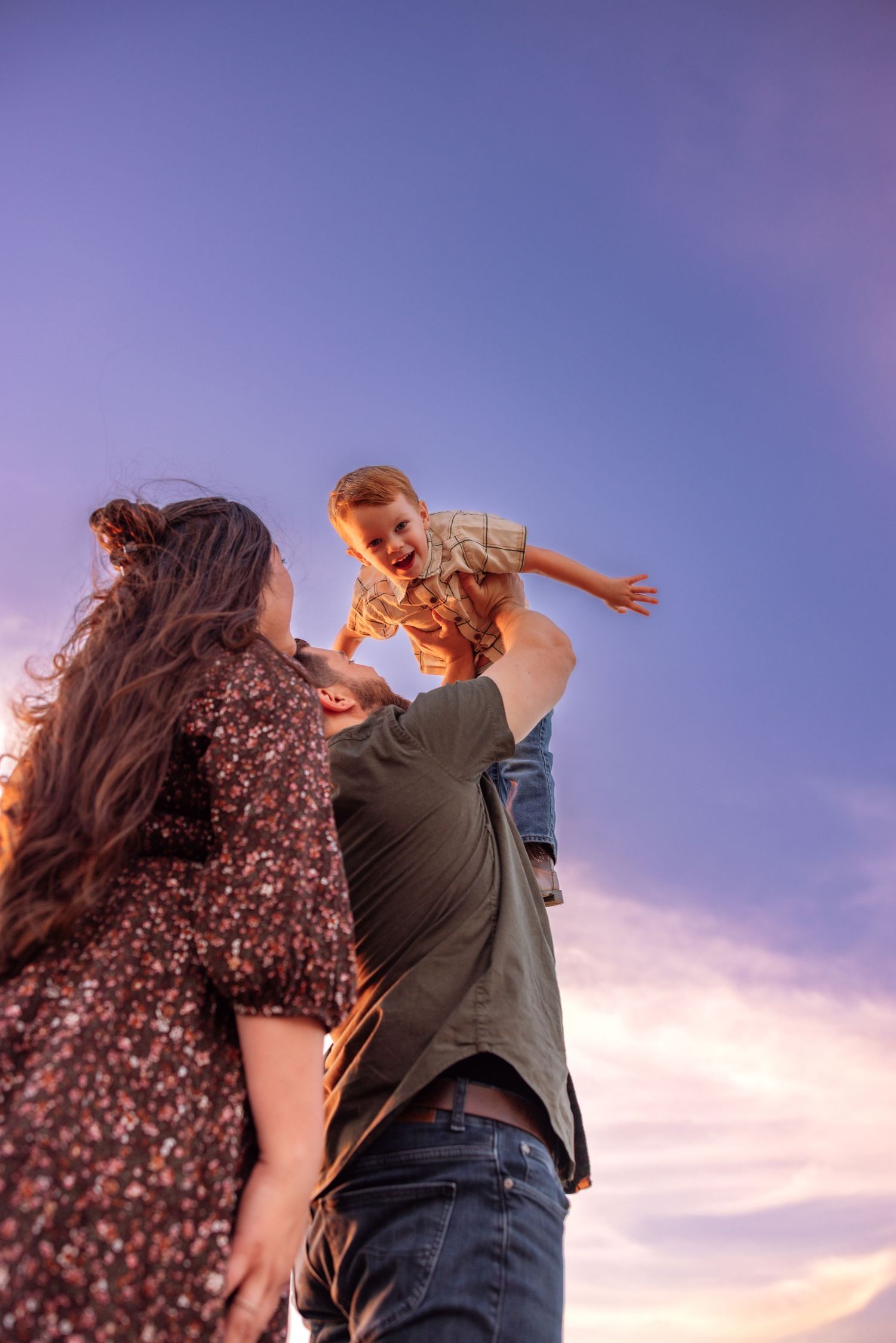 A joyful family moment at sunset as a father lifts a laughing child in the air while mother watches lovingly.