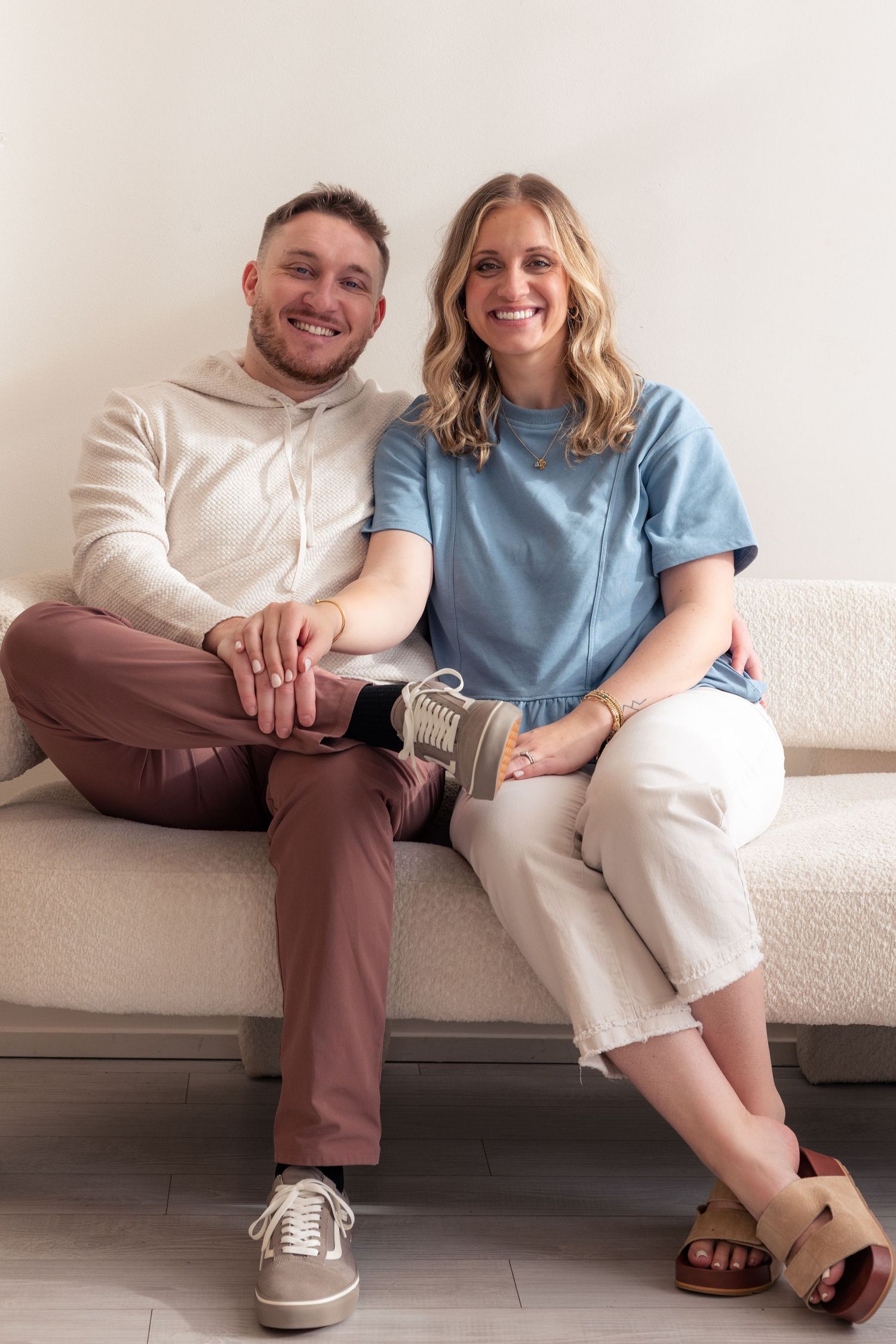 A couple sits together on a white couch, showing their casual style in matching white and blue outfits.
