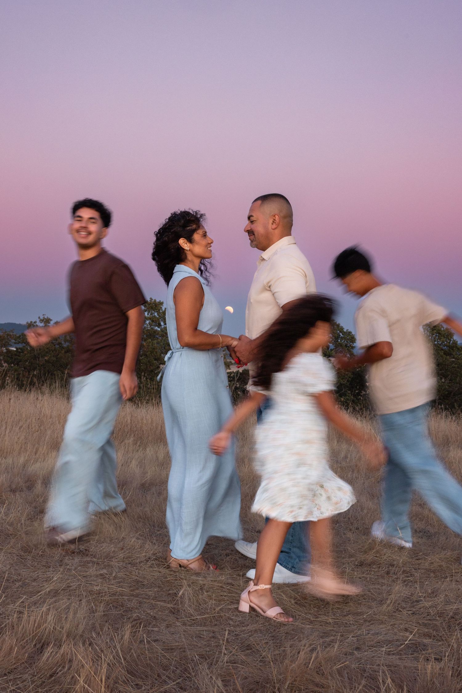 Family of five walking in a field at dusk with a pink and purple sky, captured with motion blur effect.