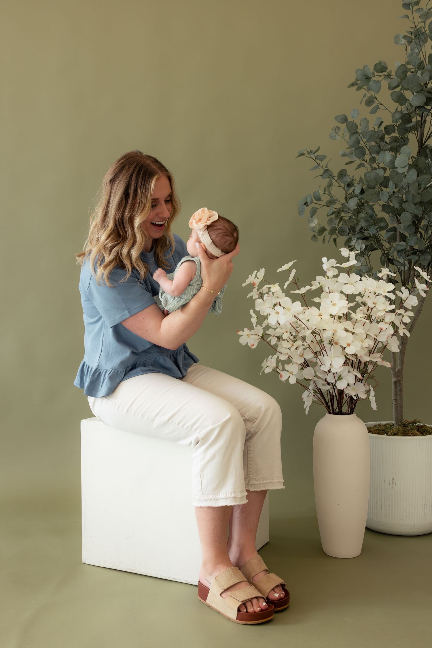 A person in a blue shirt sits with a baby on a white couch next to decorative white floral arrangements.
