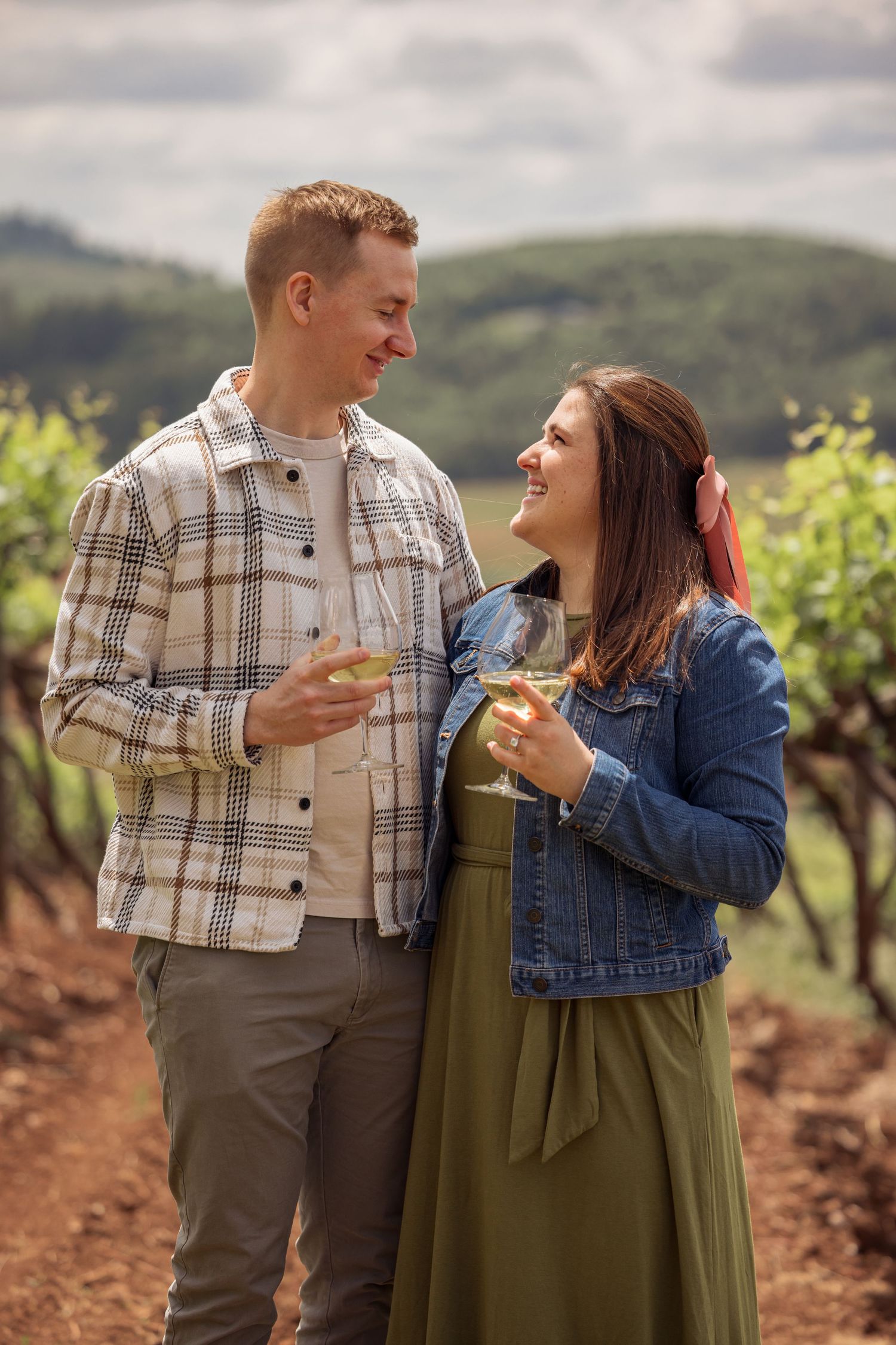Happy couple enjoying wine while standing in a scenic vineyard together on a cloudy day.