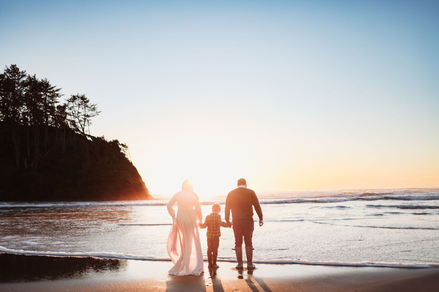 Silhouettes of a family walking together on a beach at sunset with waves crashing on the shore.