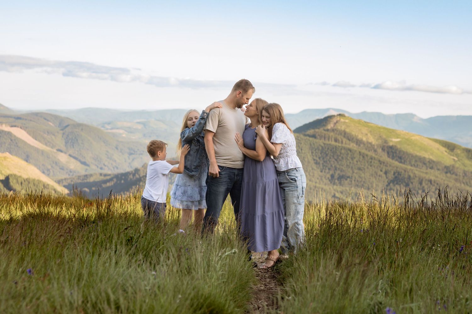 Family embracing on a mountain hilltop with scenic green valleys and blue sky in the background.