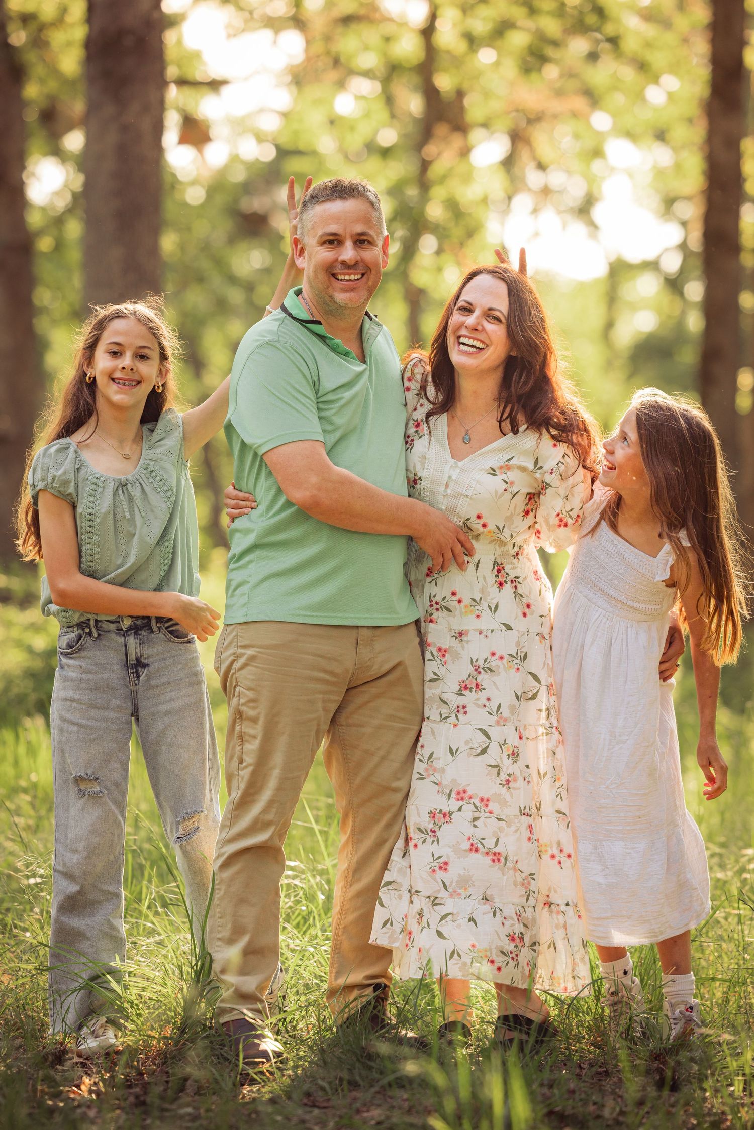 A family photo session in a sun-dappled forest with everyone wearing coordinating green and white outfits.