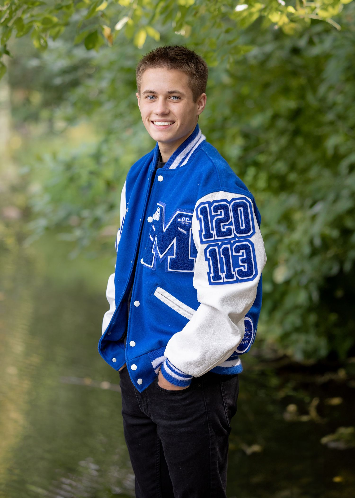Senior modeling a blue varsity letterman jacket with white lettering in an outdoor setting taken by Salem, Oregon senior photographer.