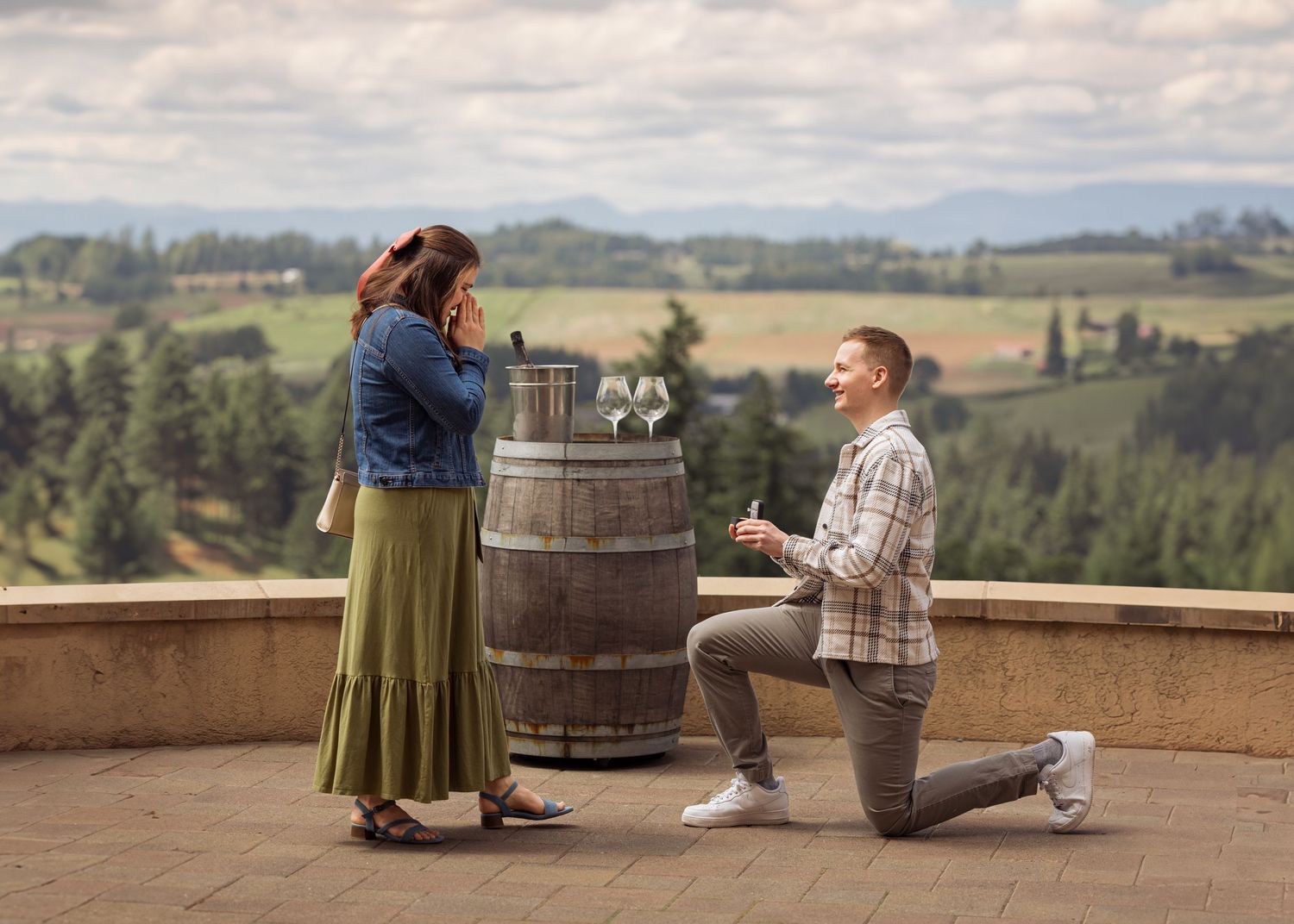 A romantic proposal moment on a winery terrace overlooking rolling hills and vineyards on a cloudy day.