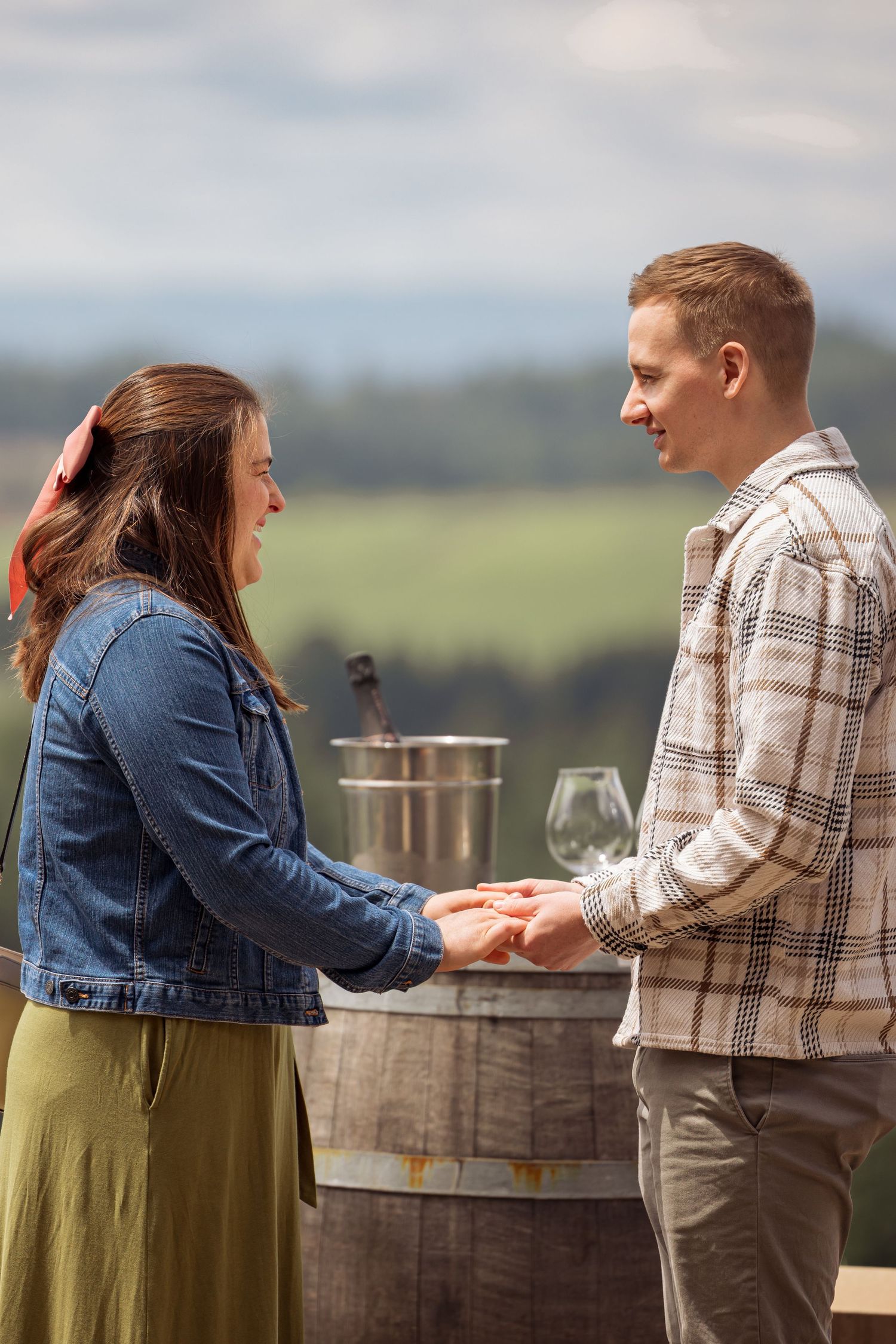 Two people sit together at an outdoor wine tasting venue with glasses and scenic views in the background.