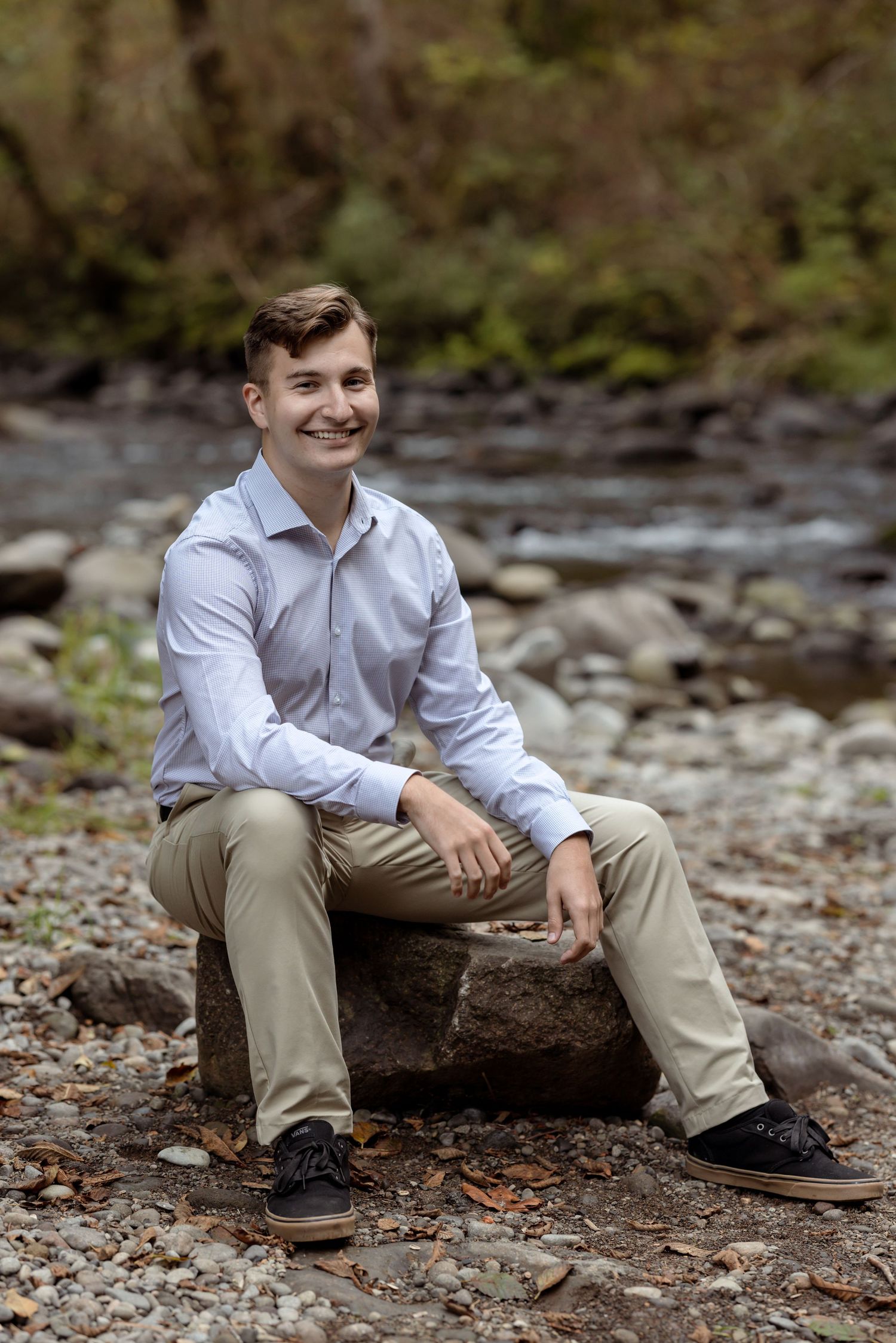 Senior l in business casual attire seated on rock by mountain stream during a photo session taken by Salem, Oregon senior photographer.