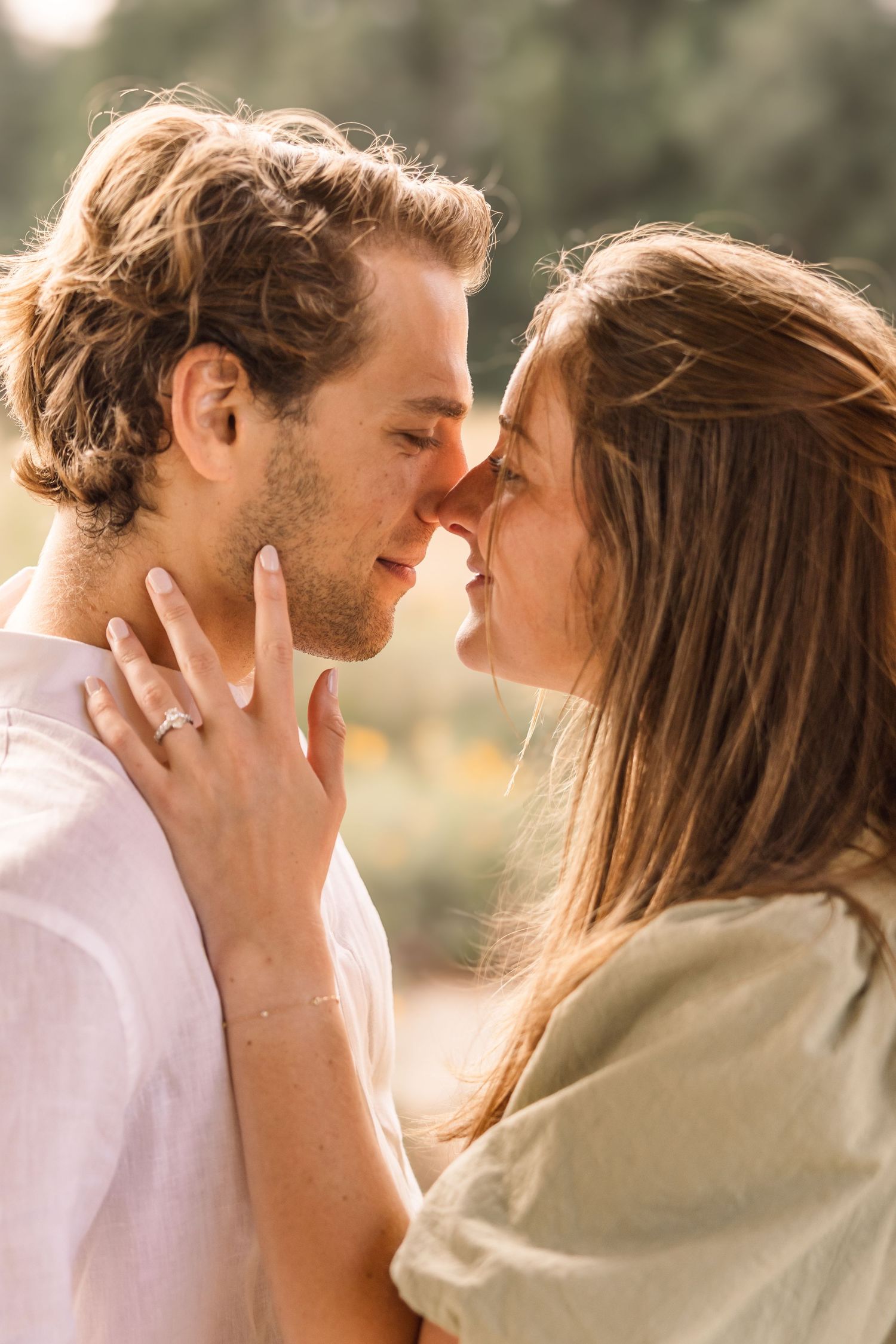 Romantic couple sharing an intimate moment outdoors, touching foreheads, woman wearing engagement ring in warm sunlight.