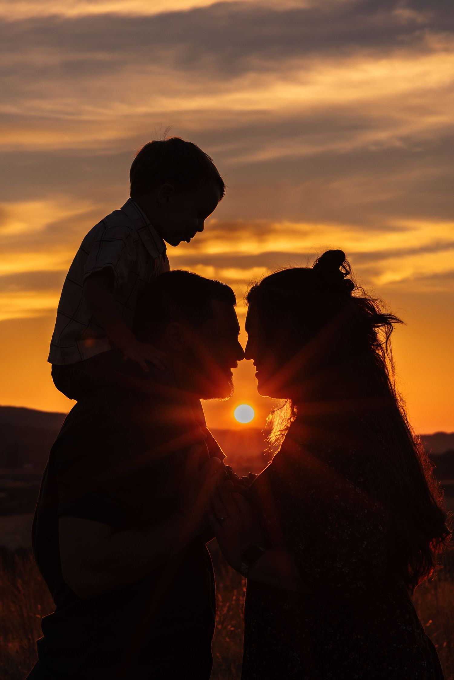 Silhouette of a family with child on shoulders against a vibrant golden sunset sky.