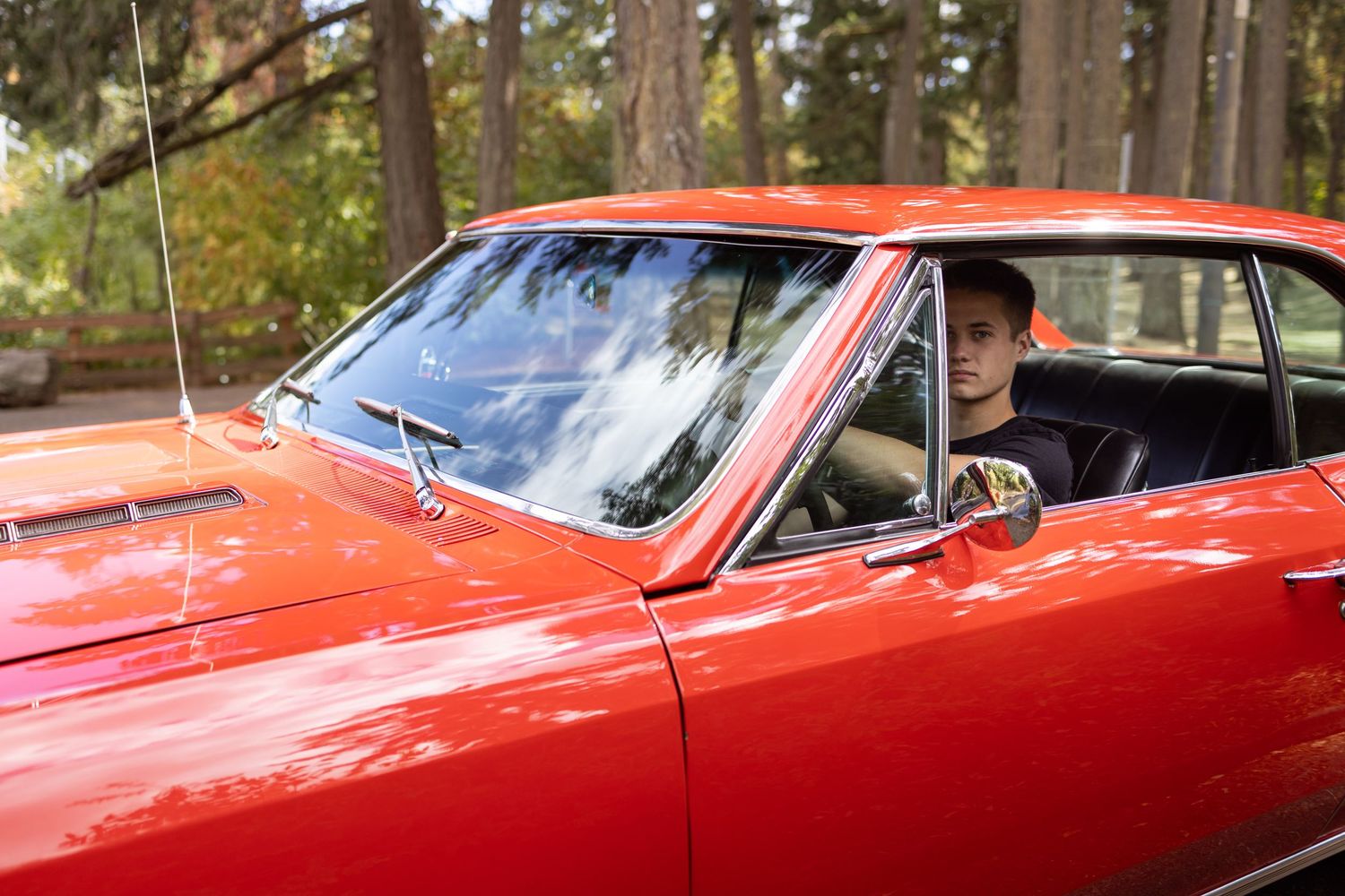 A bright red classic car with chrome trim parked in a wooded area on a sunny day taken by Salem, Oregon senior photographer