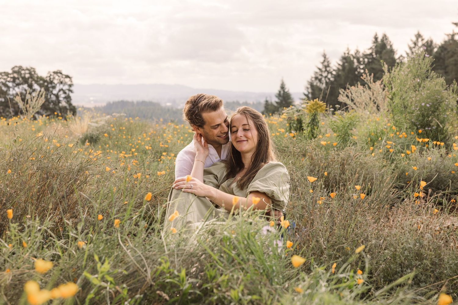 A couple shares a tender moment in a wildflower meadow during golden hour as sunlight filters through the landscape.