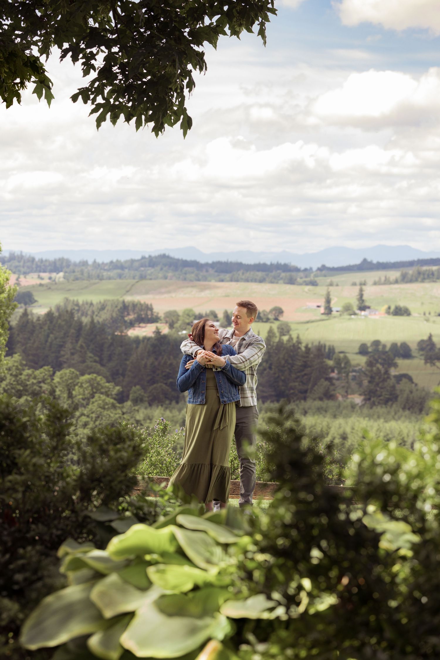 Rolling green hillsides and distant mountains provide a scenic backdrop for a tender embrace in the Oregon countryside.