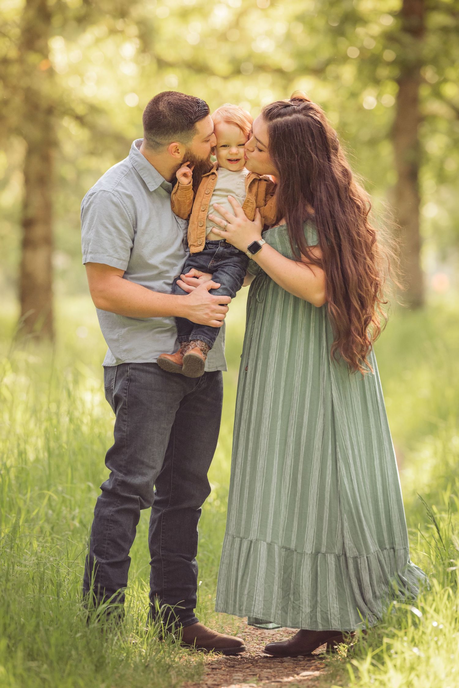 A touching sunset moment in a grassy meadow shows figures sharing sweet kisses while dressed in sage green and grey.