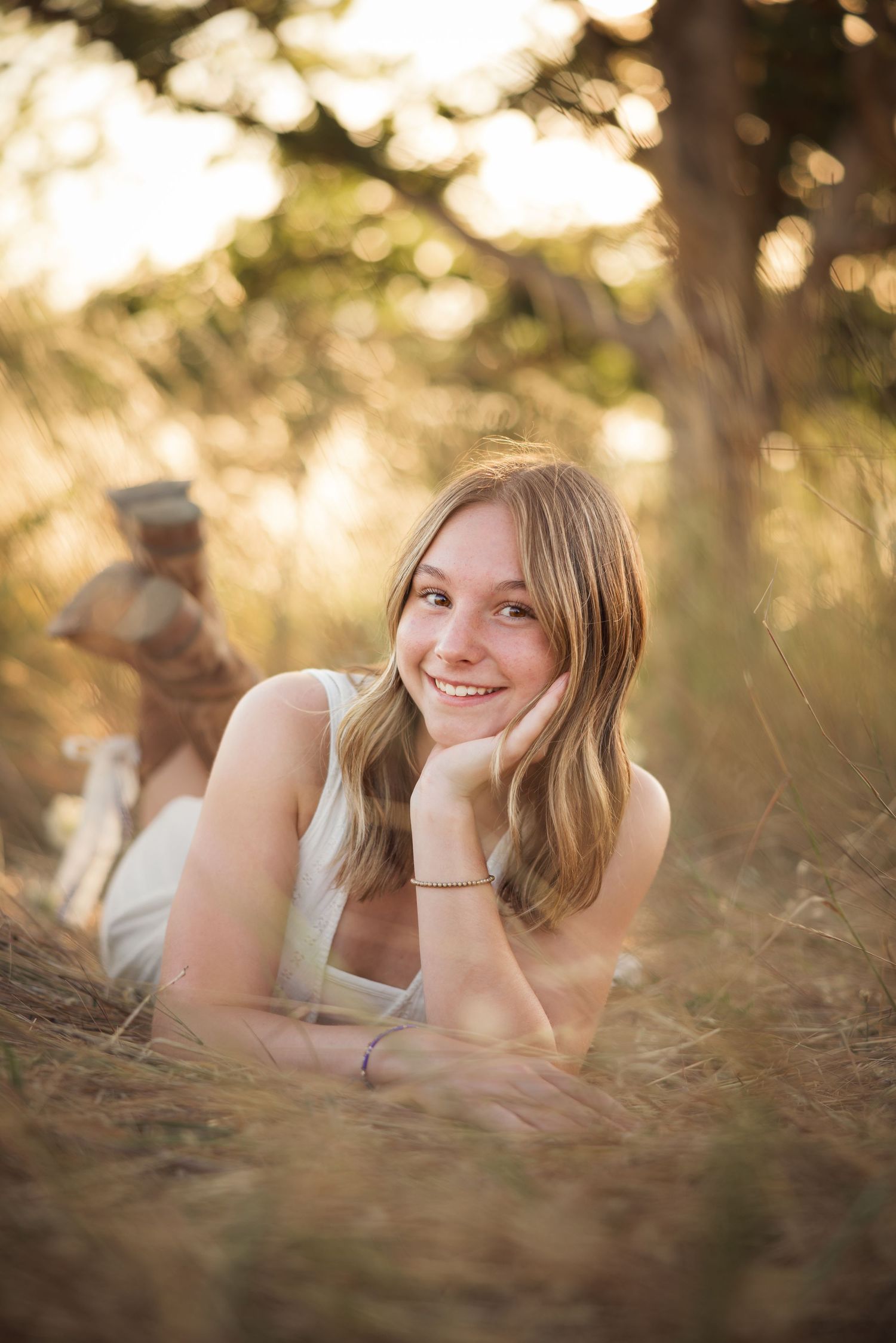 A young woman in a white top lies in golden grass during sunset, creating a dreamy outdoor portrait series.