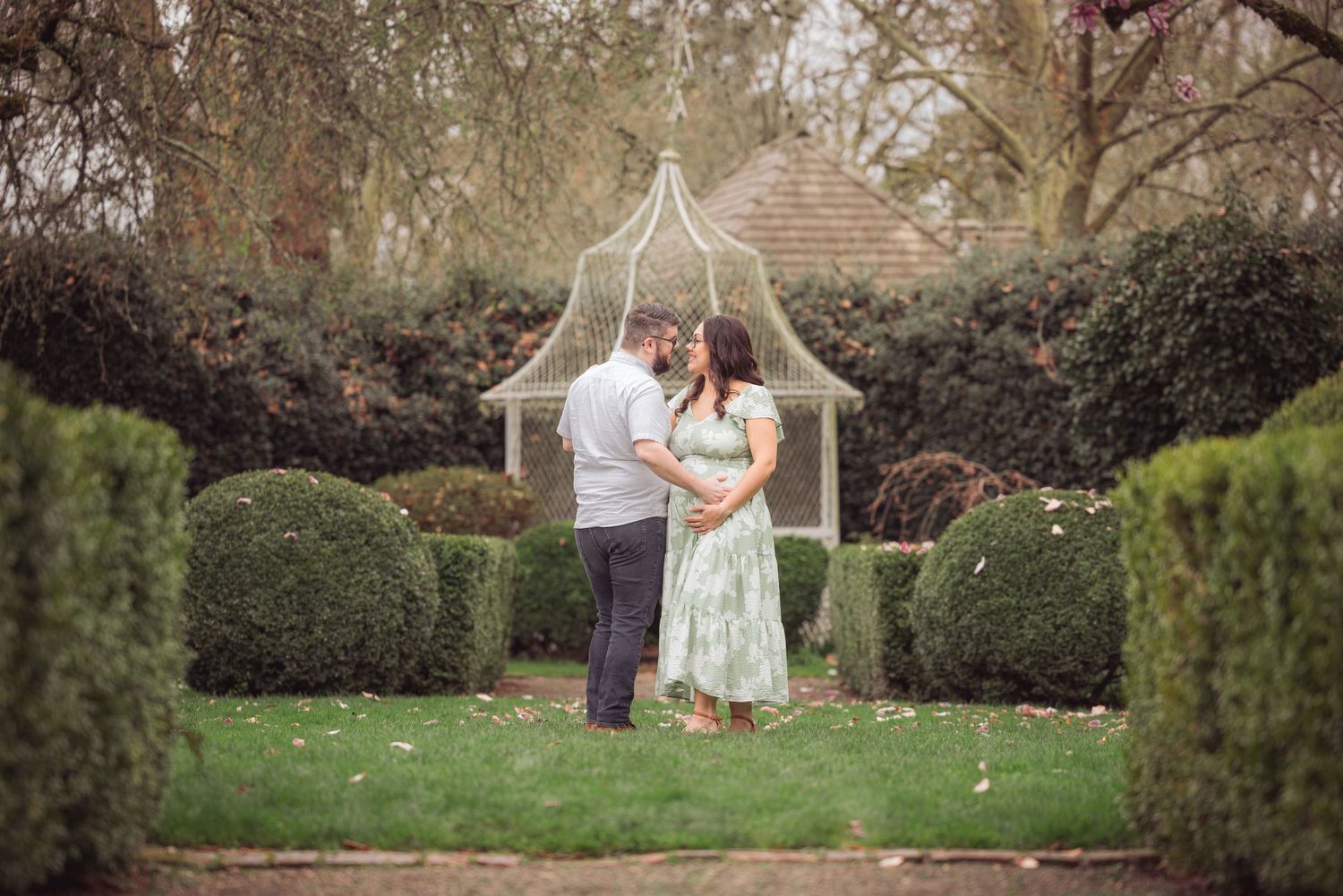 Expectant couple sharing intimate moment in garden surrounded by manicured hedges during a photo session taken by Salem, Oregon photographer