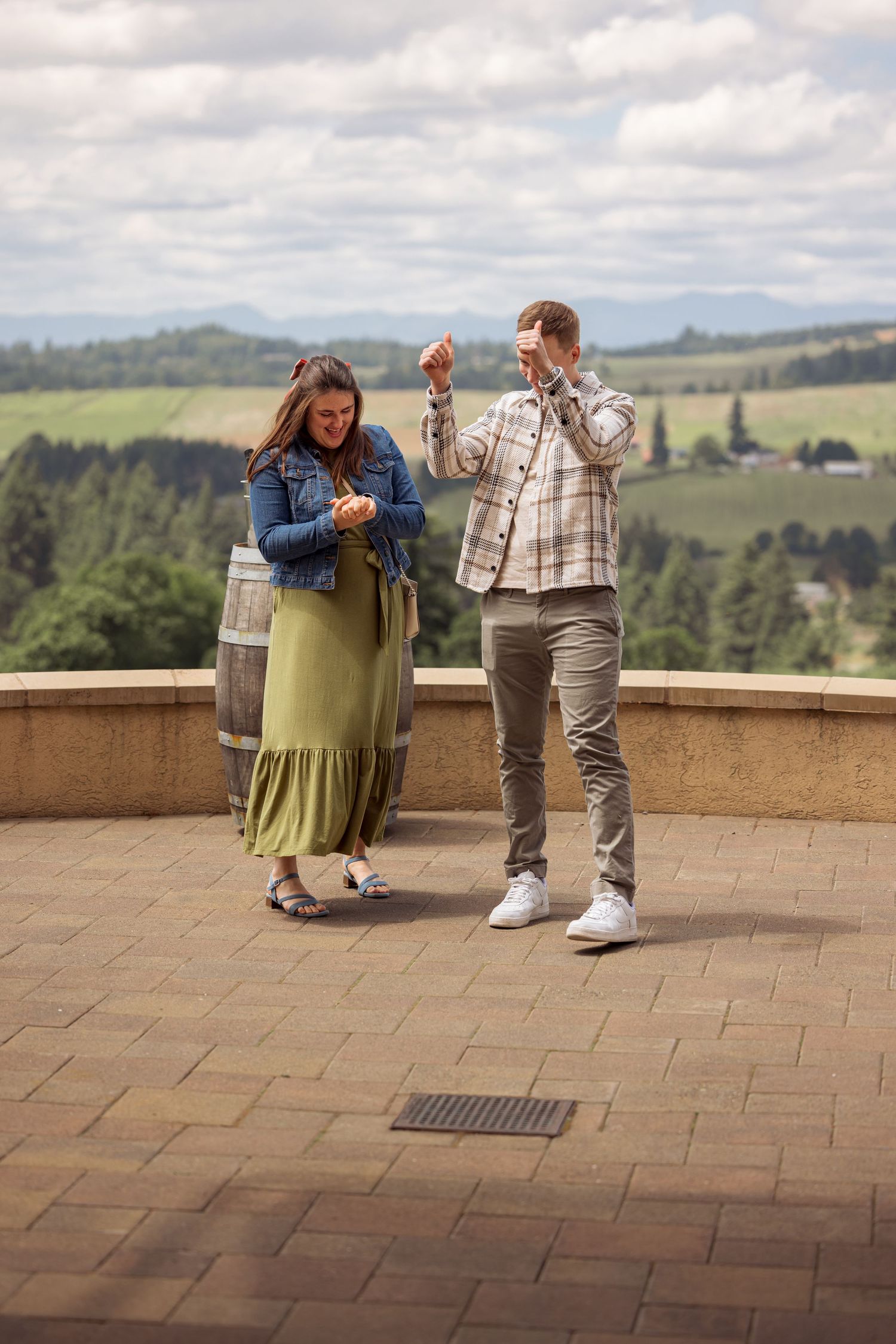 Two people enjoying wine tasting at an outdoor vineyard terrace overlooking rolling hills and countryside views.