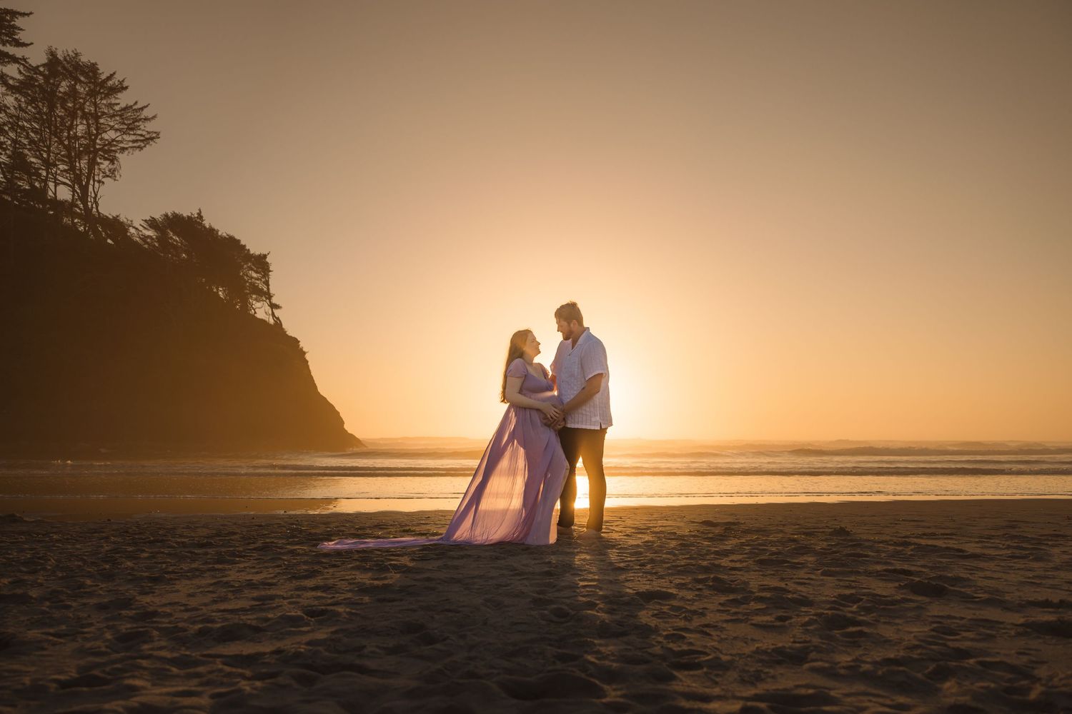 Two silhouettes stand together on a beach at sunset with golden light creating a romantic atmosphere behind them.