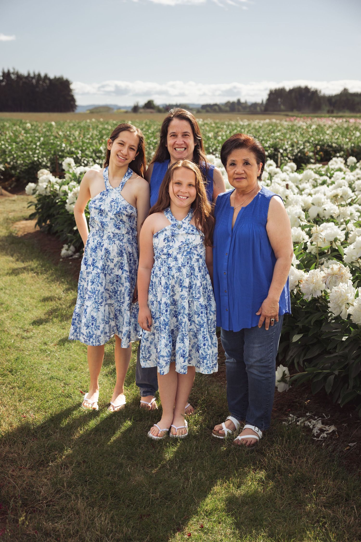 Three people wearing blue and white outfits pose together in a field of white flowers on a sunny day.