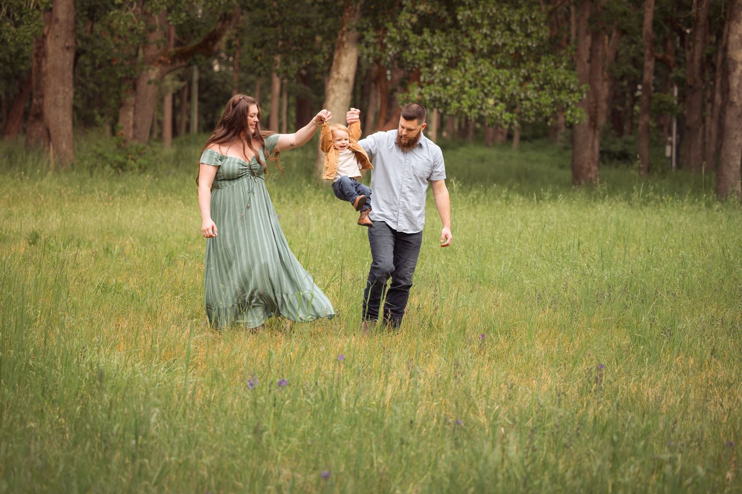 Family enjoying playful moment together in sunny meadow surrounded by pine trees.