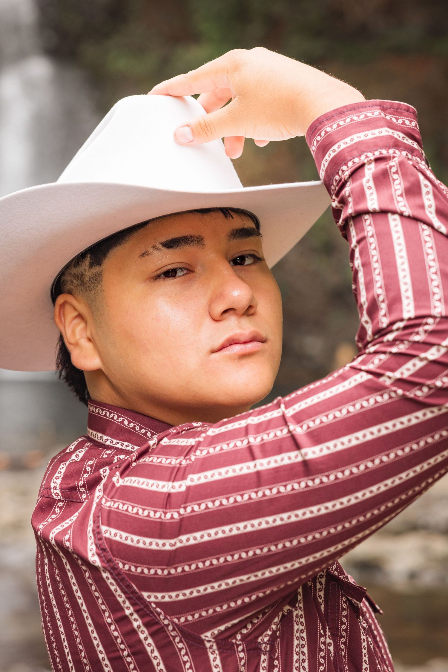 Person wearing a burgundy striped top and light colored hat poses in a series of artistic outdoor portraits.