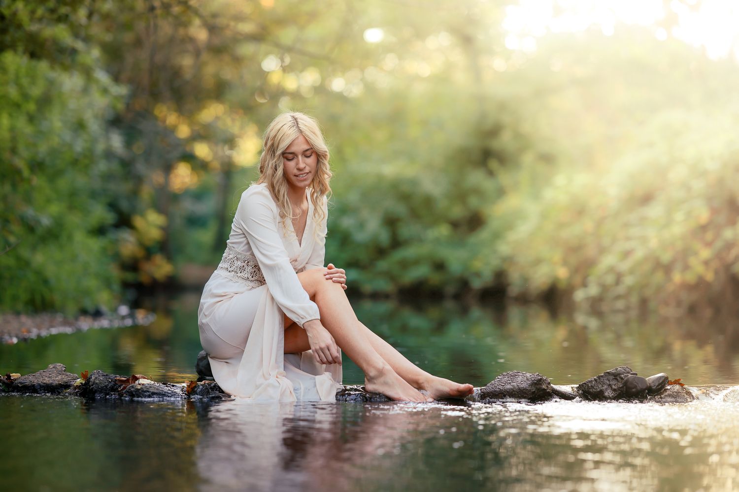 Person in white dress poses beside reflective water during sunset.