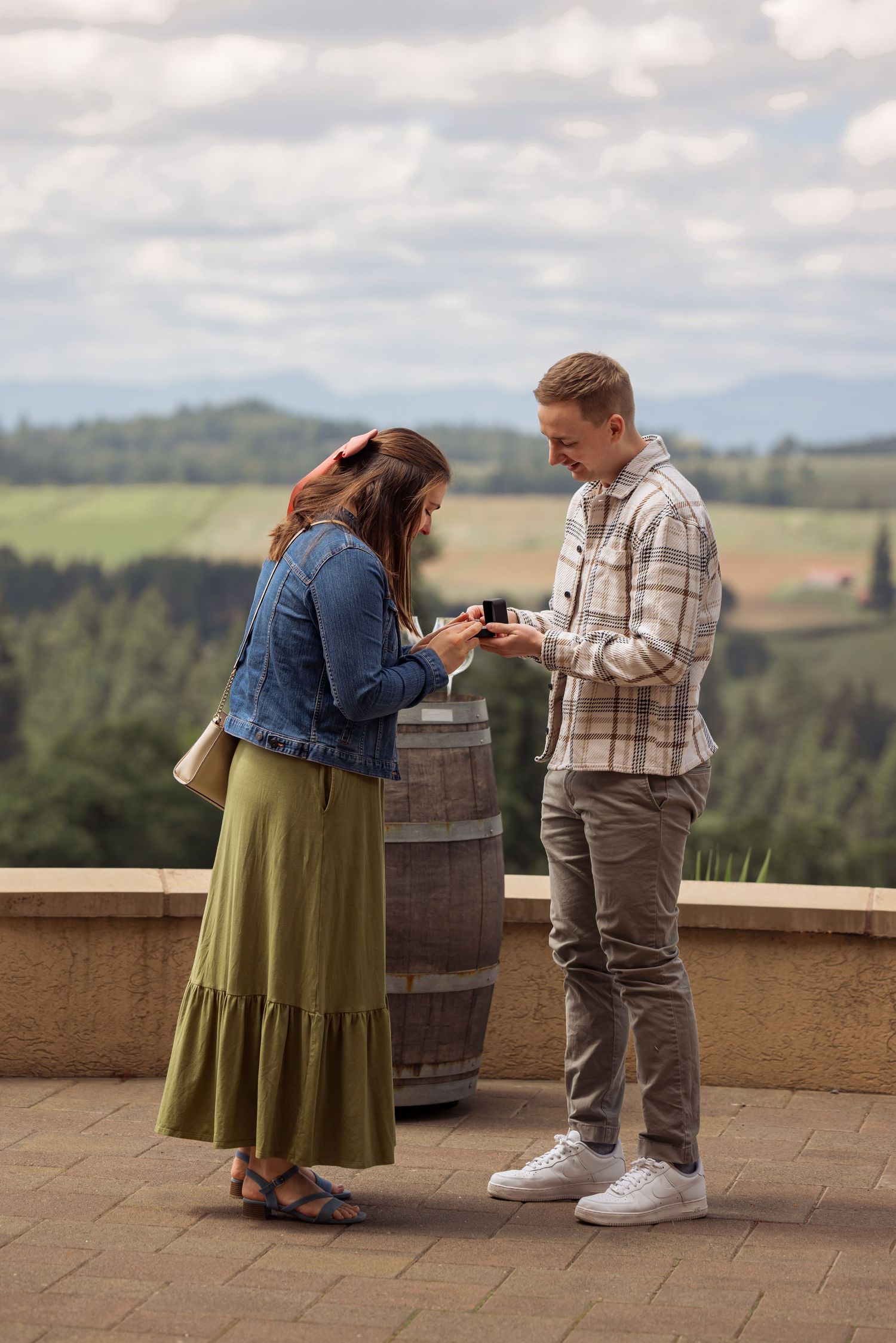 A couple exchange rings at a scenic winery overlook with rolling hills and mountains in the background.