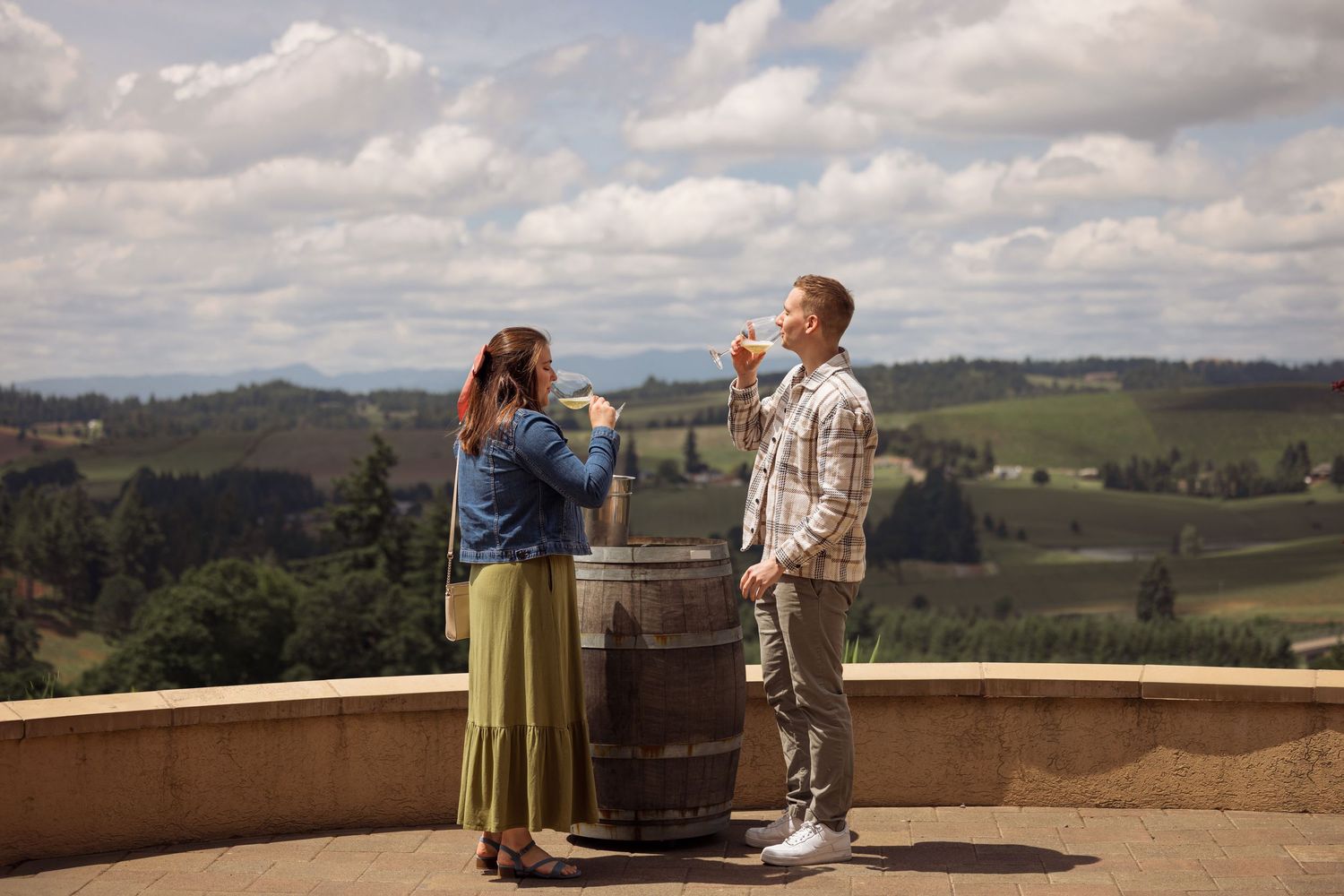 Couple enjoying panoramic views from a winery terrace overlooking scenic rolling hills on a sunny afternoon.