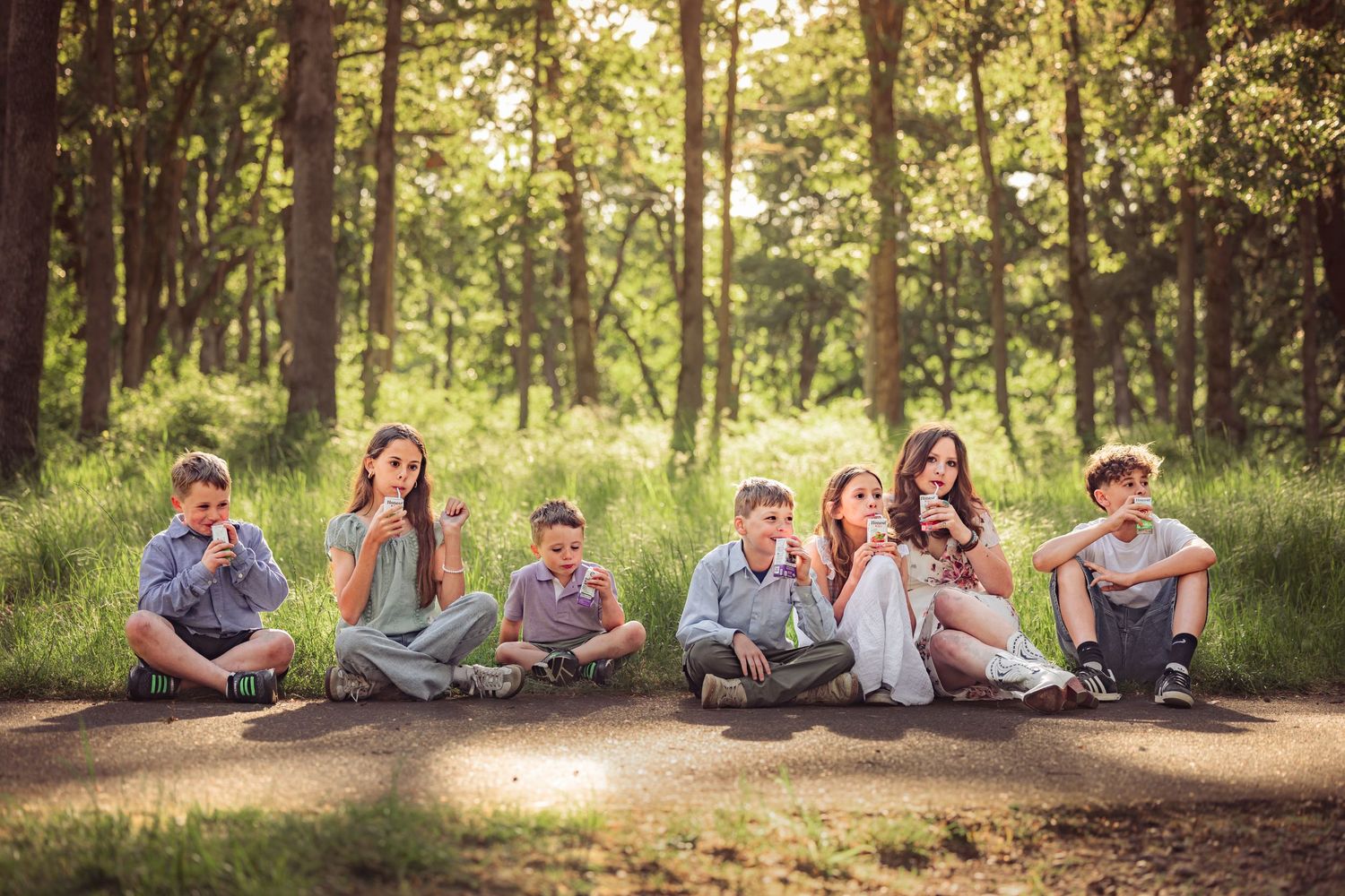 A group of young people sit together on a sunlit forest path while enjoying apples in a peaceful woodland setting.