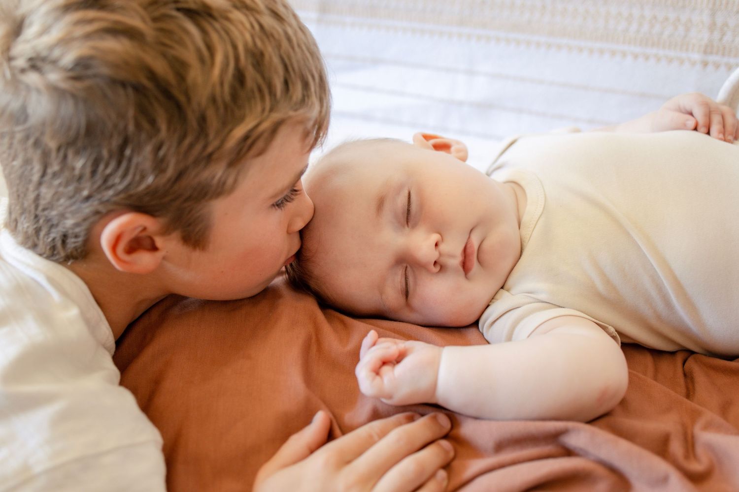 Two children sharing tender moment while resting on orange bedding during a photo session taken by Salem, Oregon family photographer.