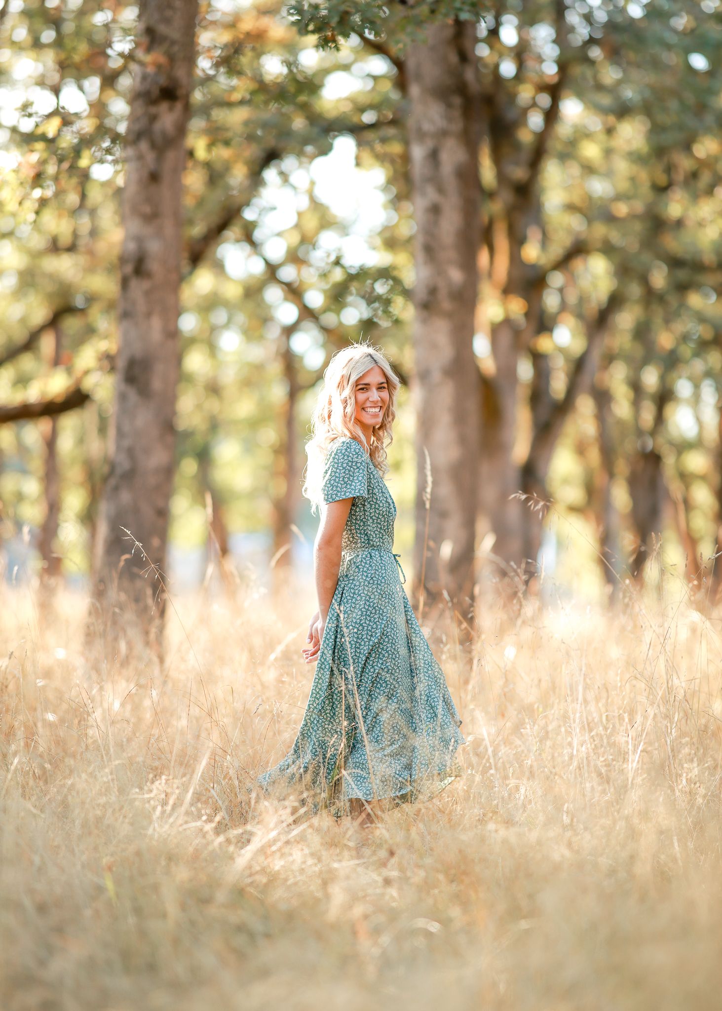 Senior in a flowing dress stands in a golden field during a photo session taken by Salem, Oregon senior photographer.