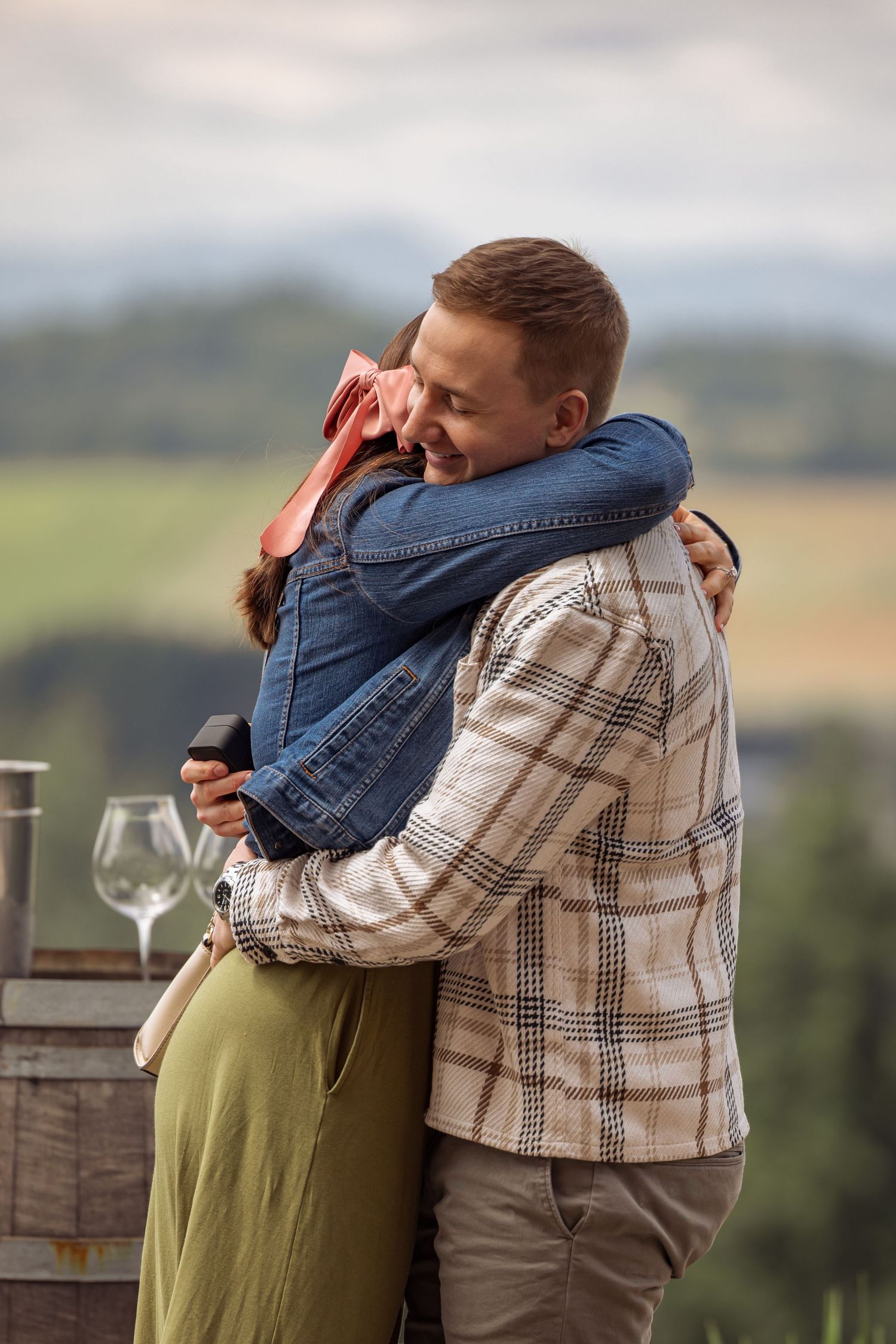 A couple share an intimate embrace on an outdoor terrace overlooking a scenic valley landscape.