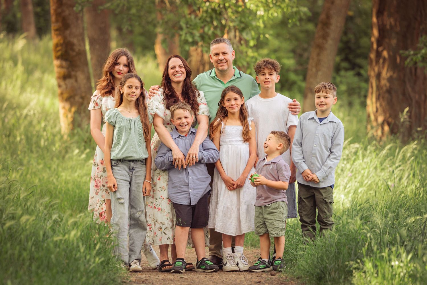 Family group portrait on forest path with sunlight filtering through trees during a photo session by Salem, Oregon family photographer.