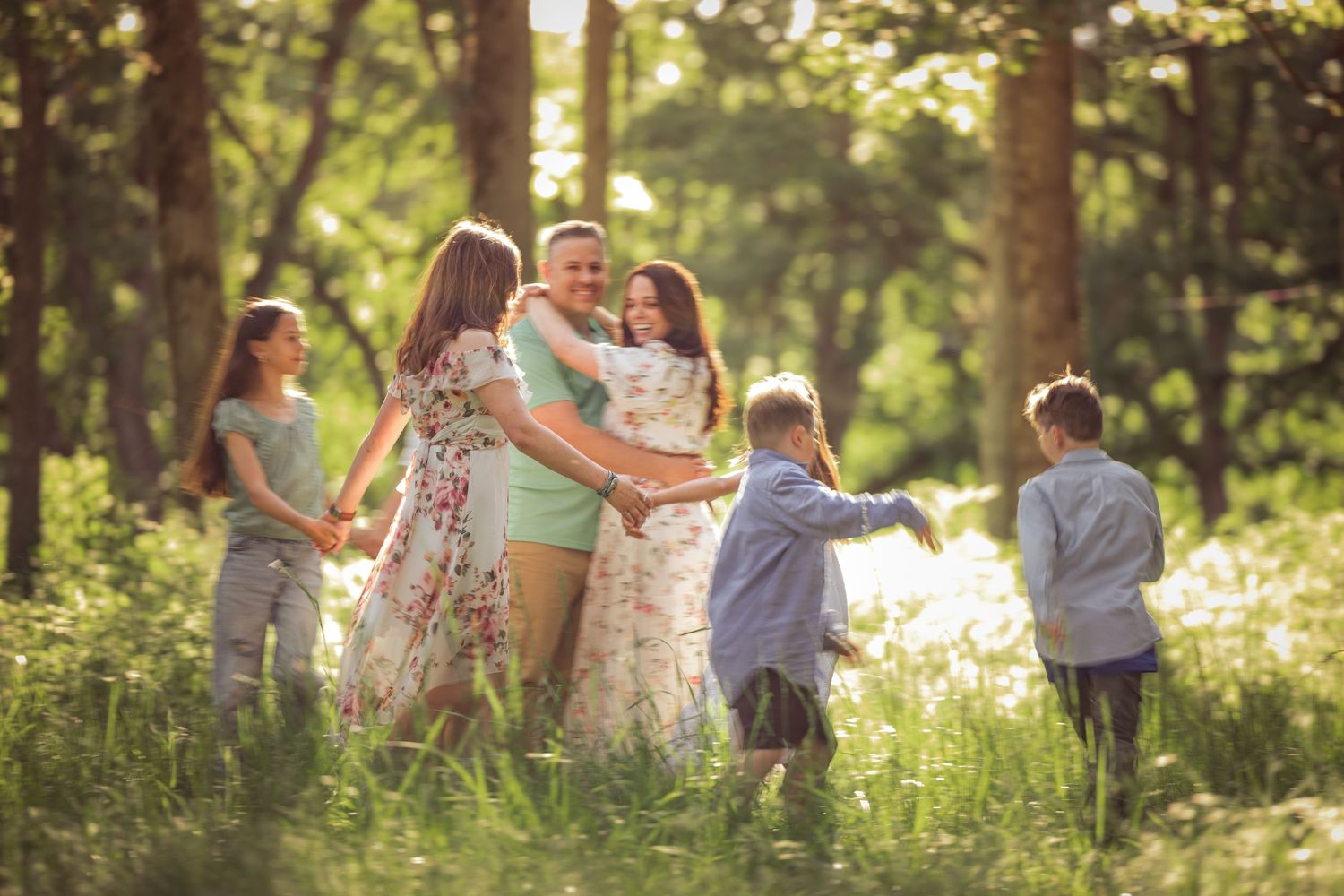 People joyfully dance together in a sunlit forest clearing during a celebratory outdoor gathering taken by Salem, Oregon family photographer