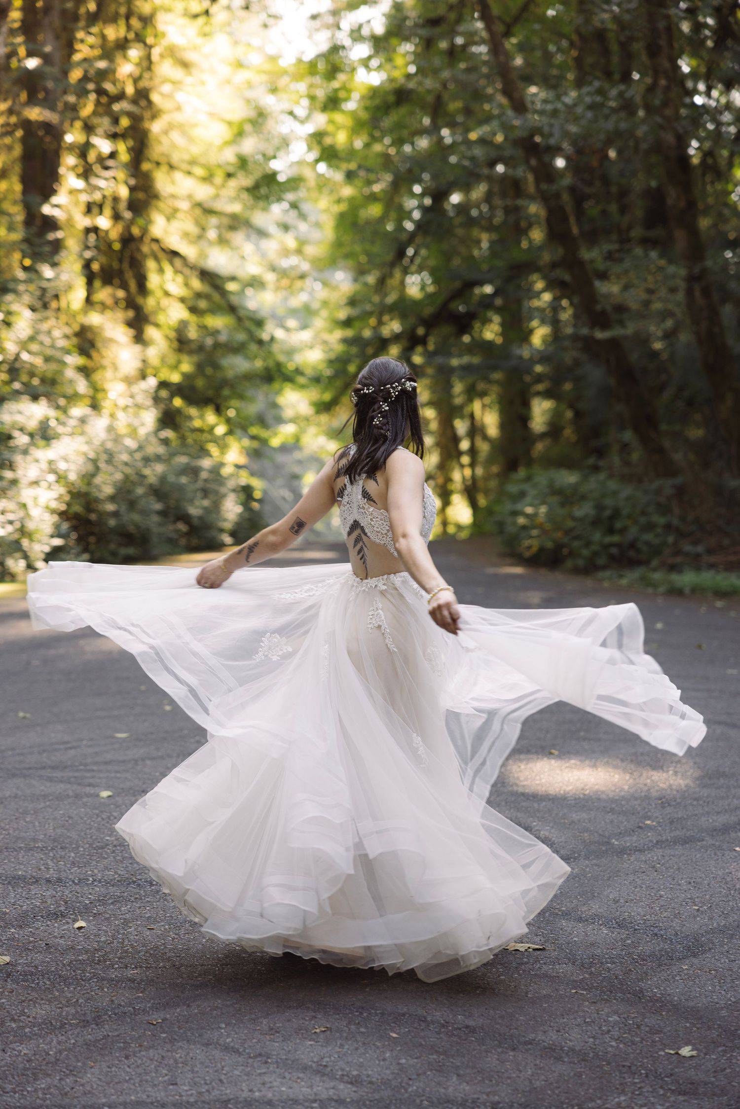 Bride in flowing white boho gown twirling on a forest road, dress billowing gracefully, with floral hair crown.