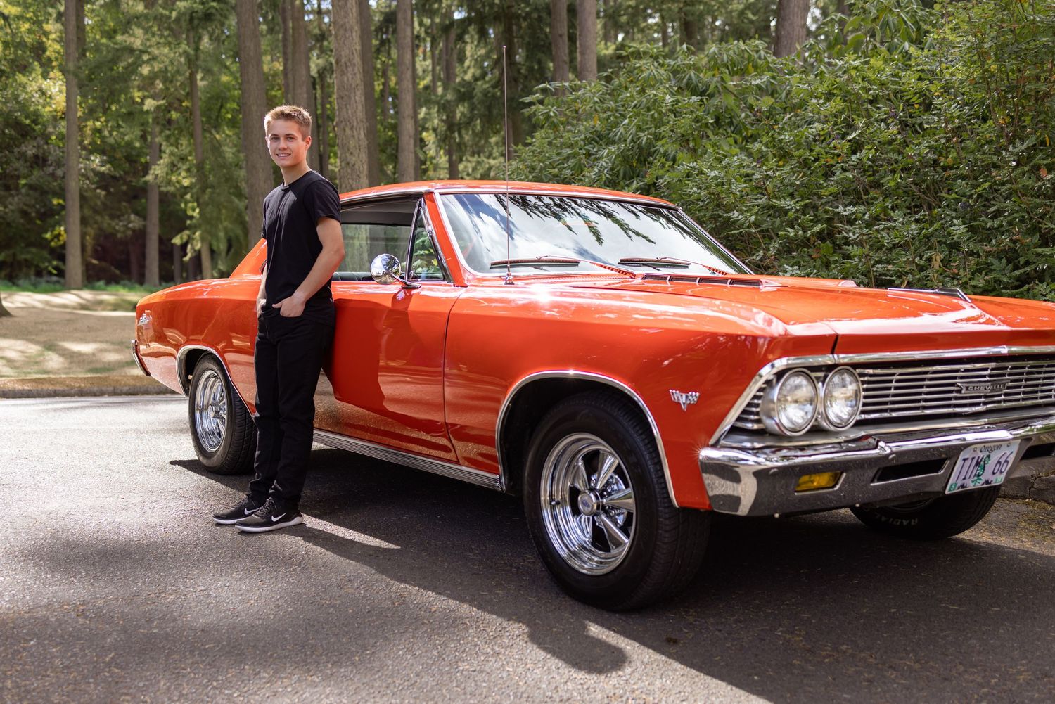 A classic red Chevrolet Chevelle muscle car parked in a forested area during a photo session taken by Salem, Oregon senior photographer.