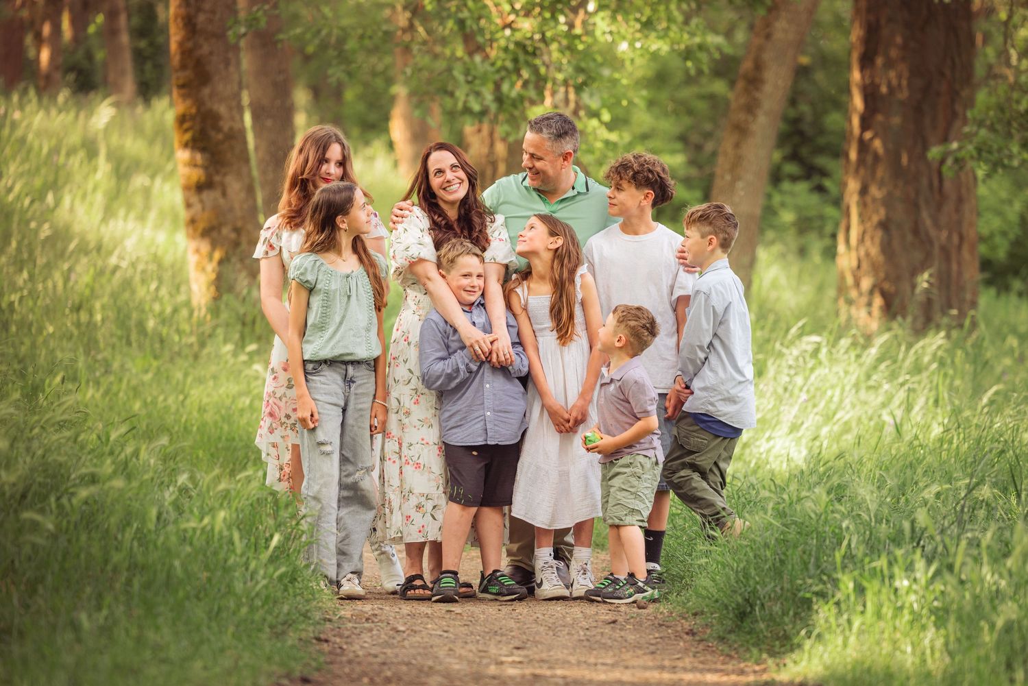 Family walks through a sunlit wooded path during a summer photo session.